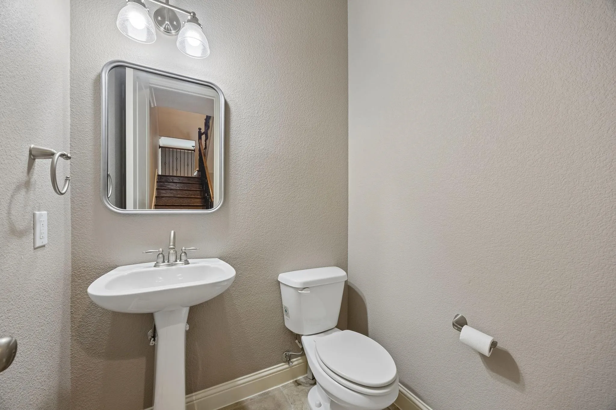 Pedestal sink with a polished chrome faucet, rectangular framed mirror, and two-light vanity fixture