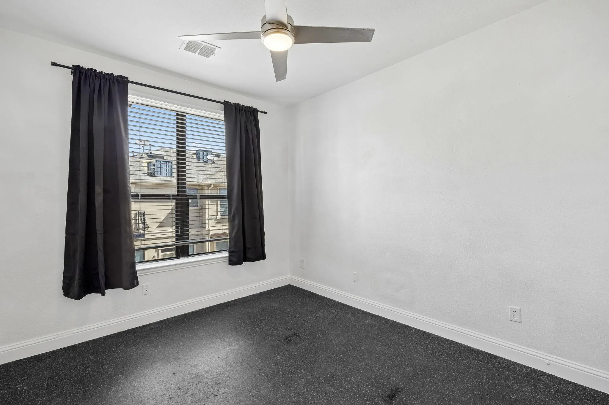 Window with horizontal blinds, overhead ceiling fan, and dark carpeting