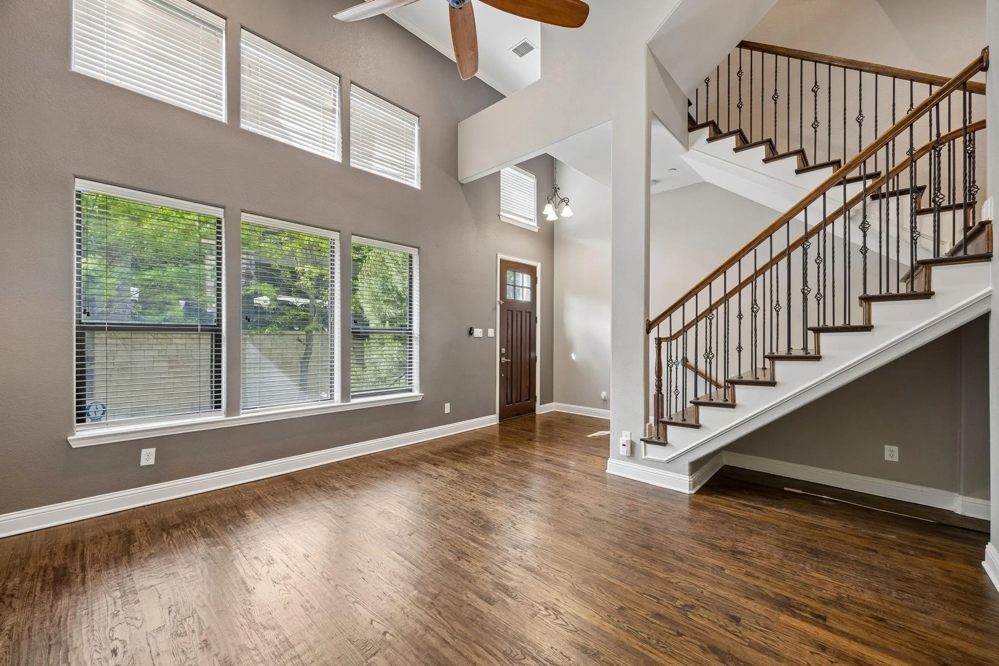 Vaulted ceiling with a ceiling fan, wood-finish flooring, multiple windows, staircase with wrought iron balusters, and a solid wood entry door