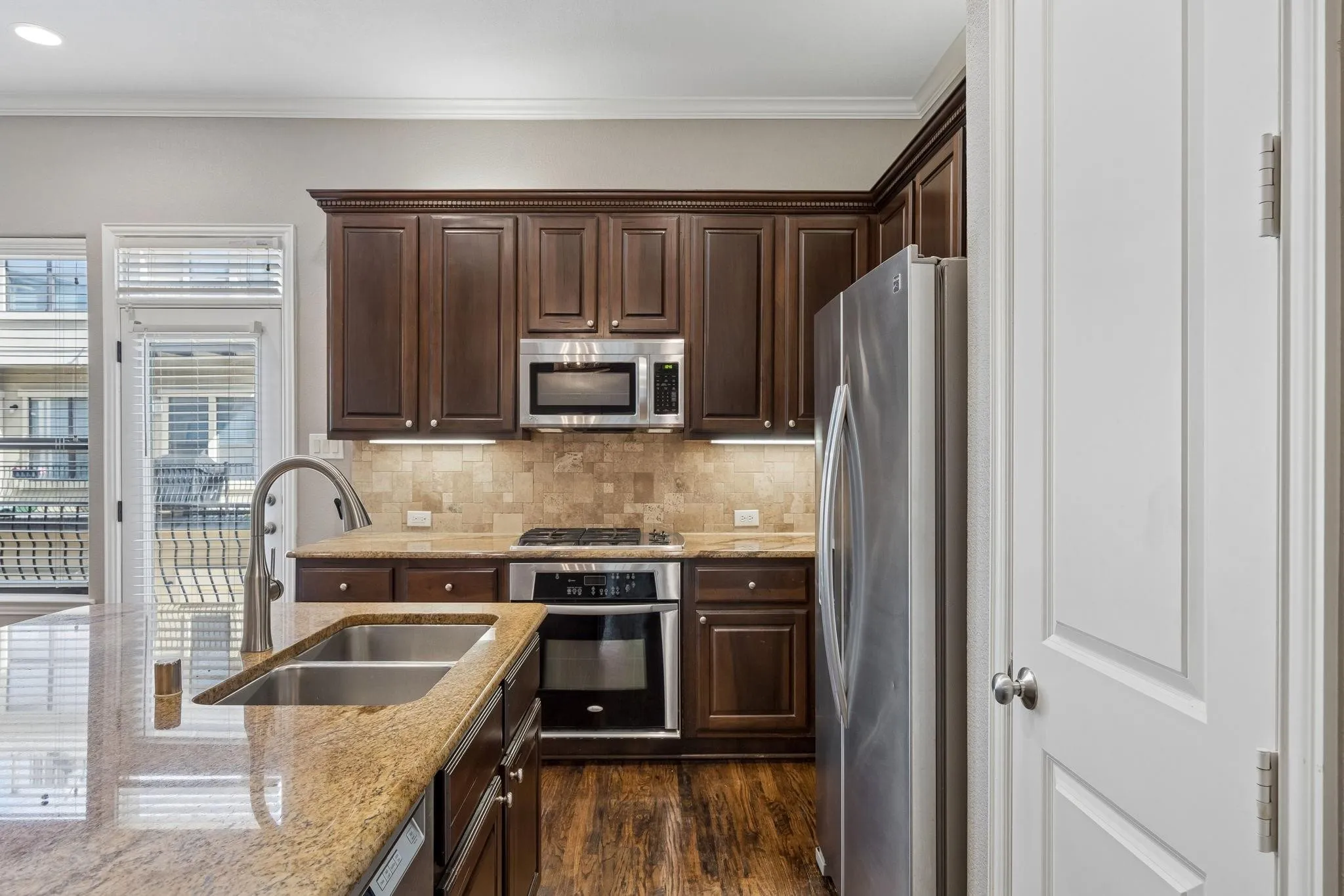 Kitchen featuring wood-finish flooring, dark wood cabinetry, granite countertops, stainless steel appliances, and a double basin sink