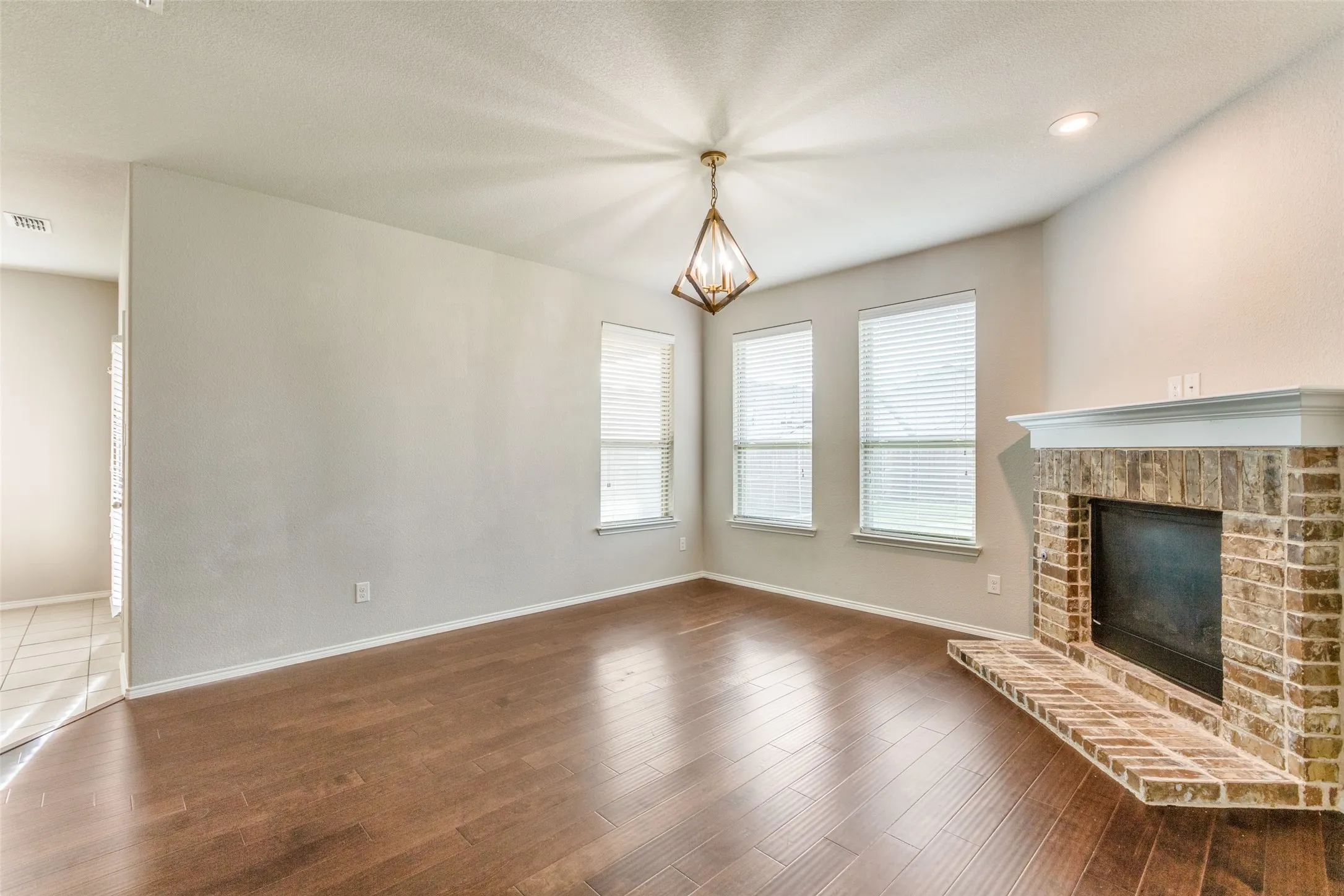 Wood-finish flooring with a brick-faced fireplace, white mantel, and three windows