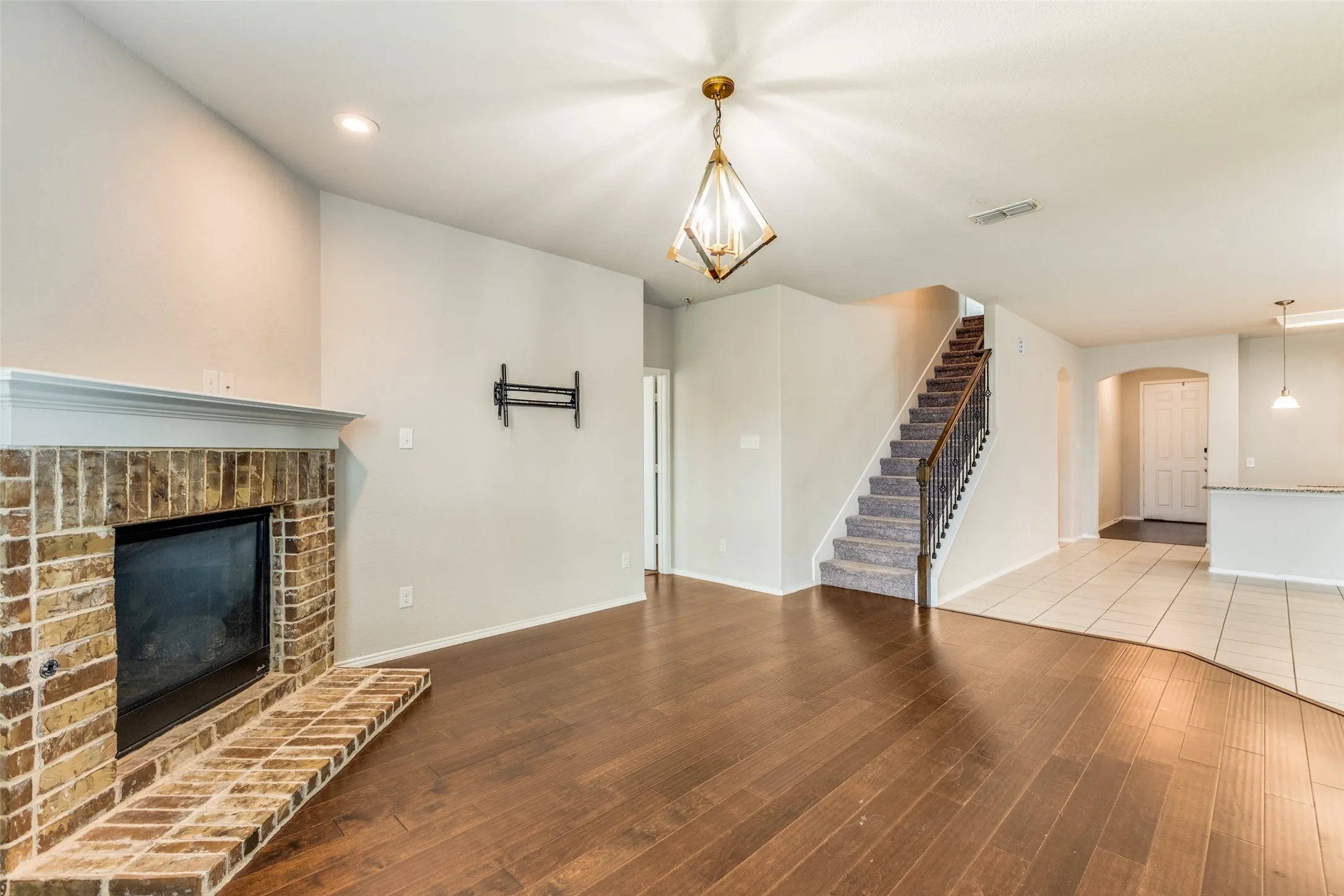 Brick fireplace with white mantle, dark wood-finish flooring, and a carpeted staircase with wrought iron balusters