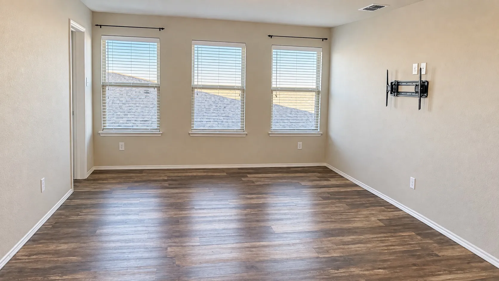 Wood-finish flooring, three windows with blinds, light neutral wall color, and a wall-mounted bracket