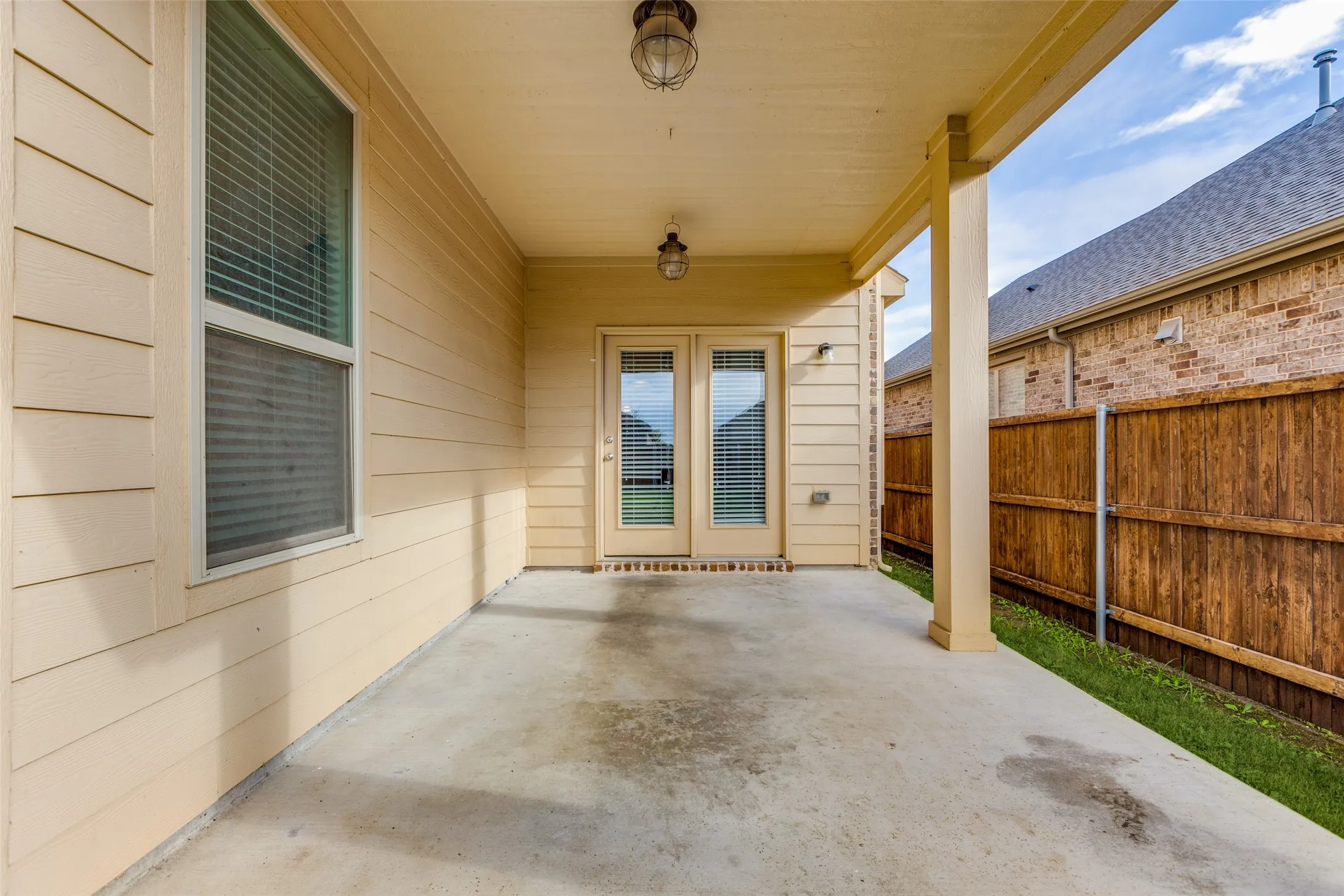 Covered patio with concrete flooring and wood-beam ceiling, featuring French doors with glass panels, sidelite windows, and direct access to the fenced backyard with wooden privacy fencing
