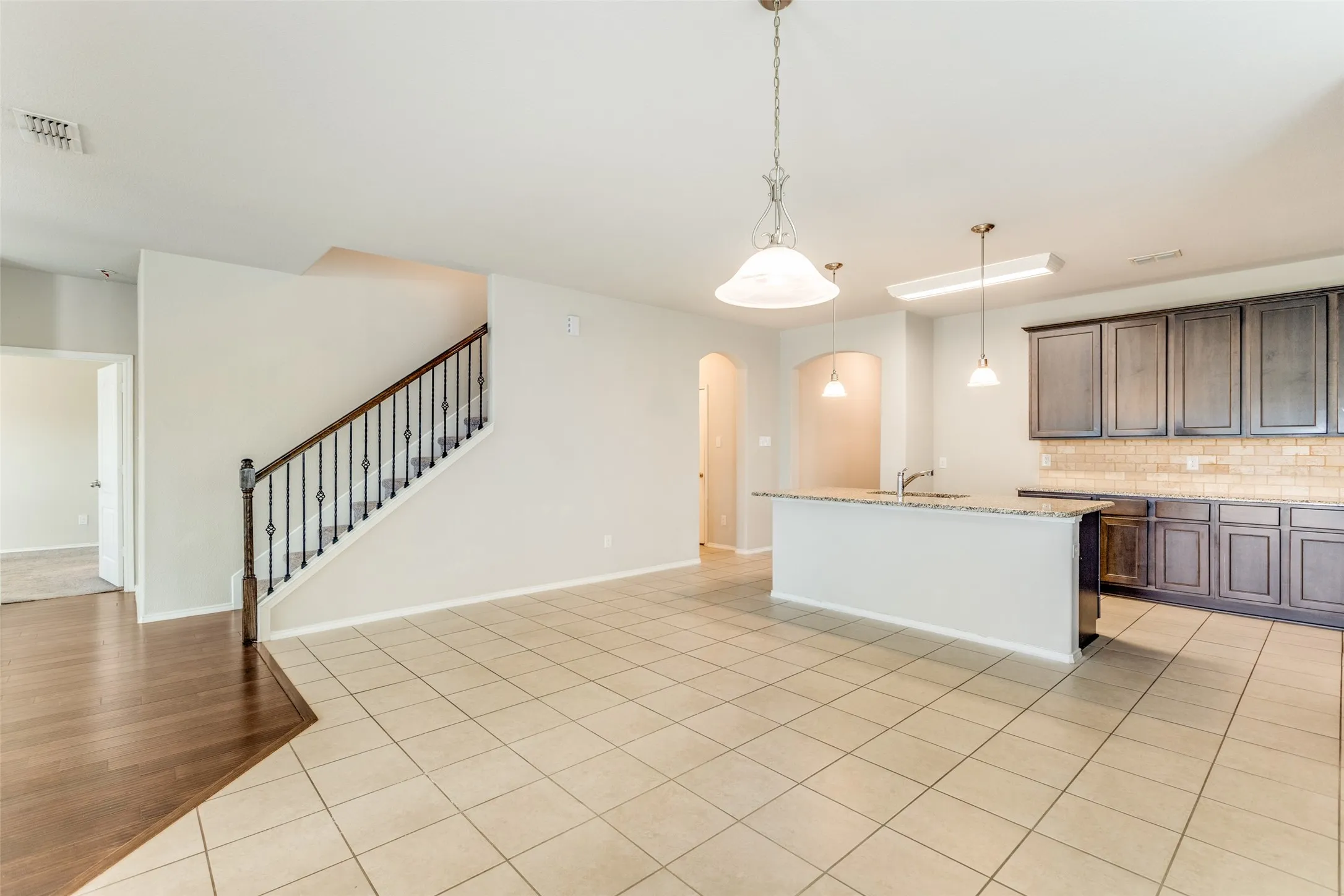 Open-concept living area with tile flooring and a staircase featuring wrought iron balusters