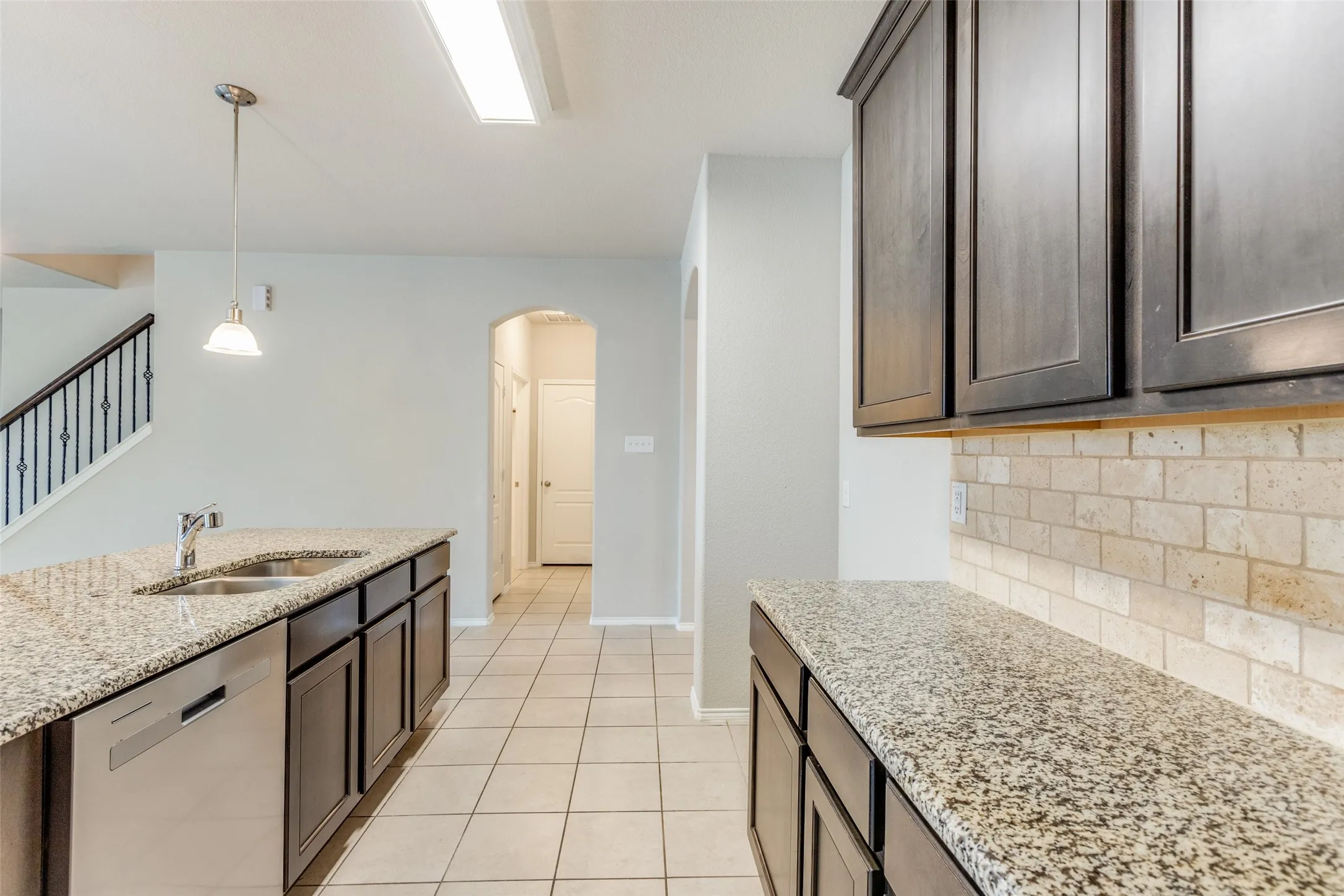 Kitchen featuring granite countertops, wood-finish cabinetry, a stainless steel dishwasher, a tile backsplash, and a ceramic tile floor
