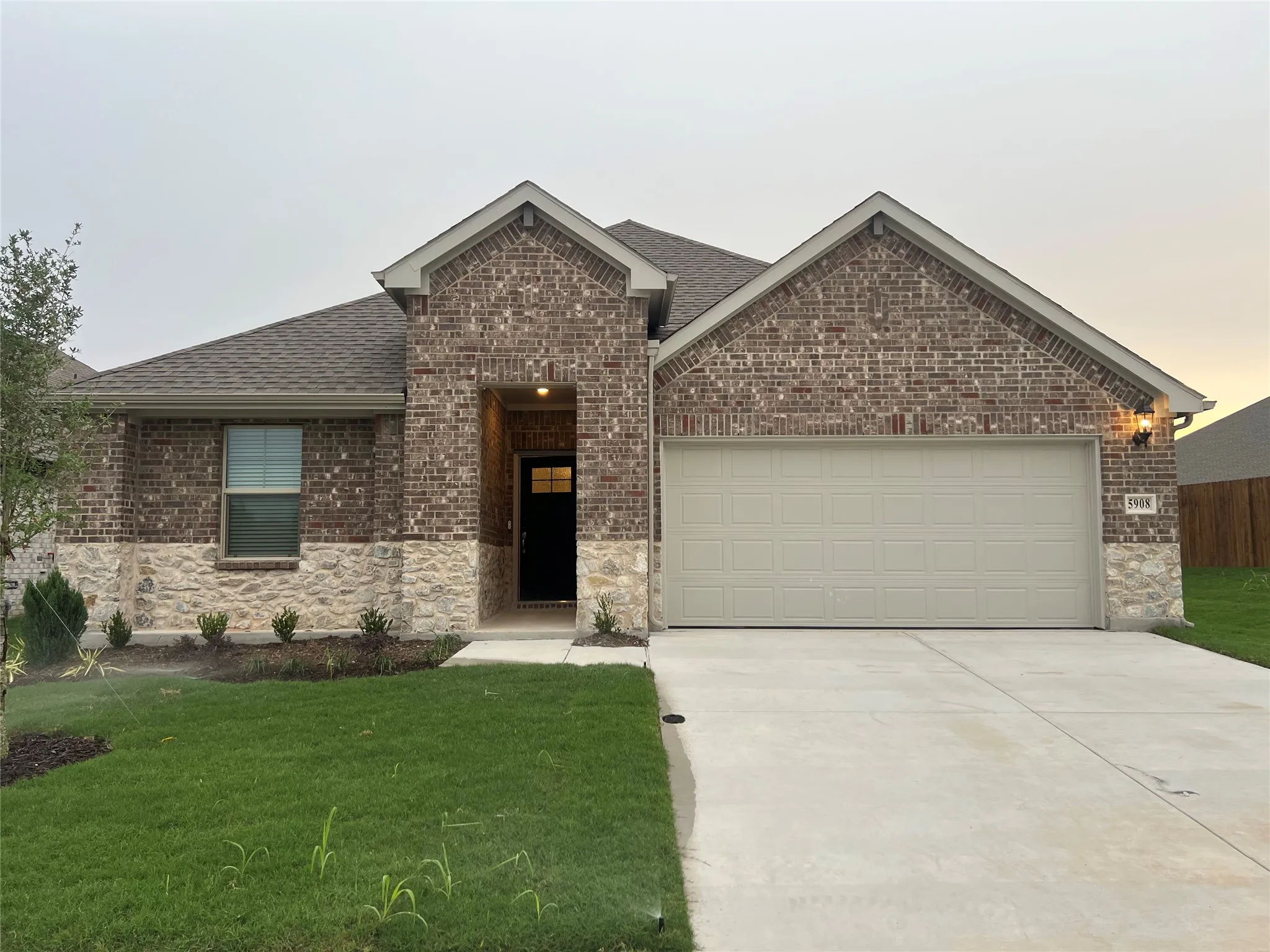 Brick and stone exterior with an attached garage, covered entry, and concrete driveway