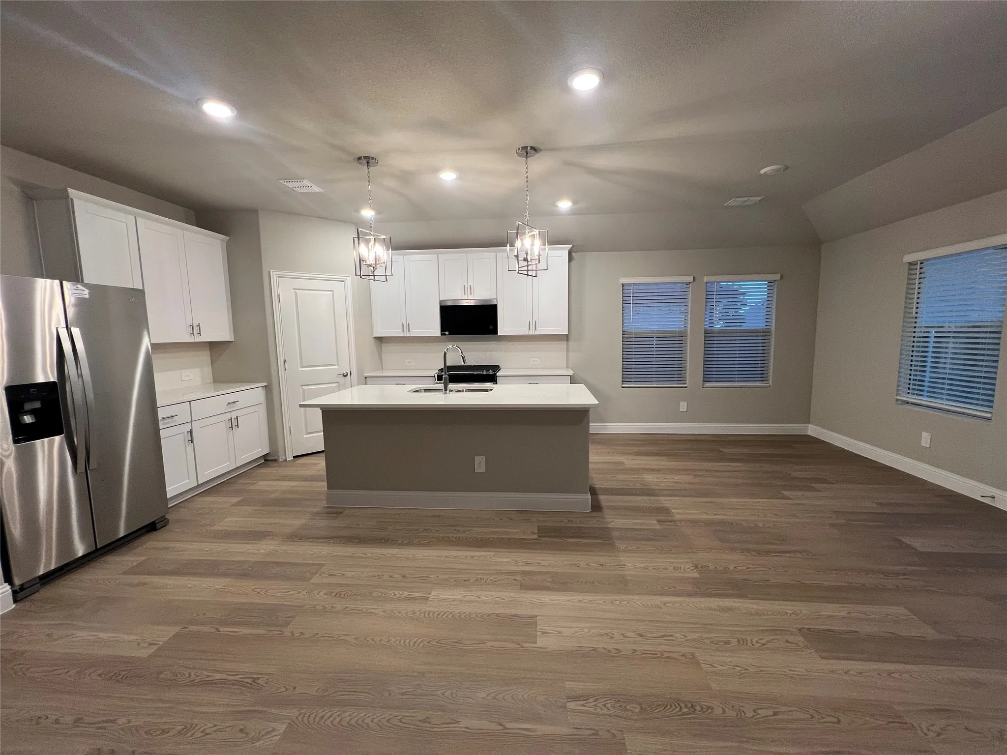Spacious open-concept living area with wood-finish flooring, recessed lighting, and a kitchen island with pendant lighting