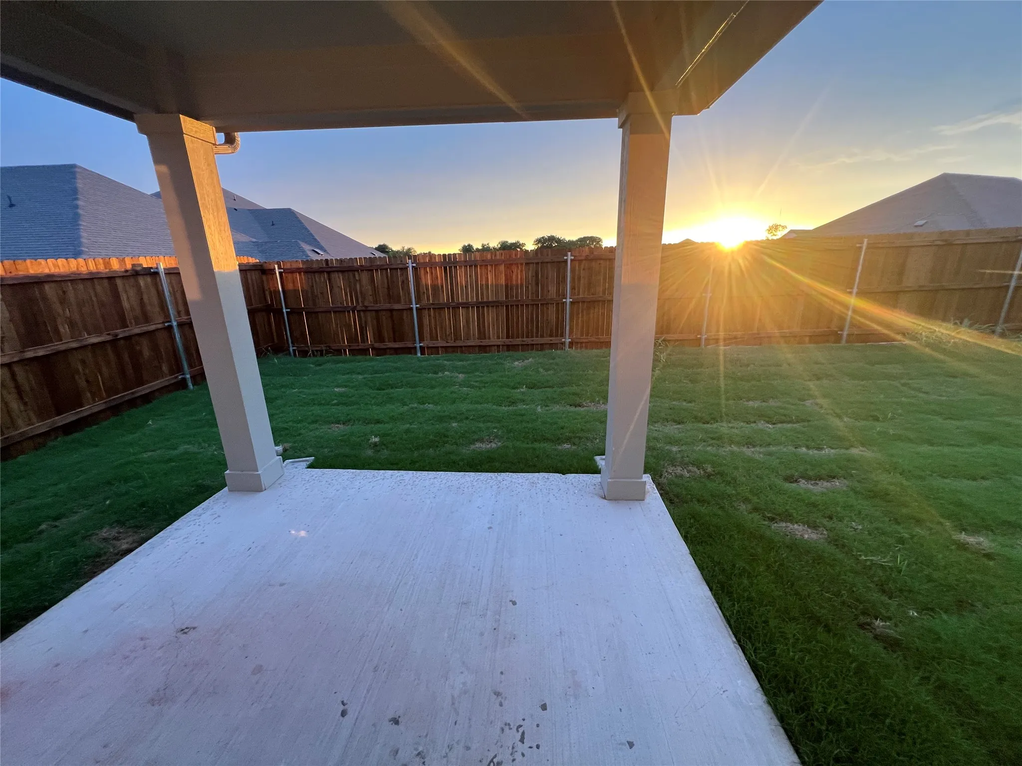 Covered concrete patio with a spacious grass lawn and wood fencing