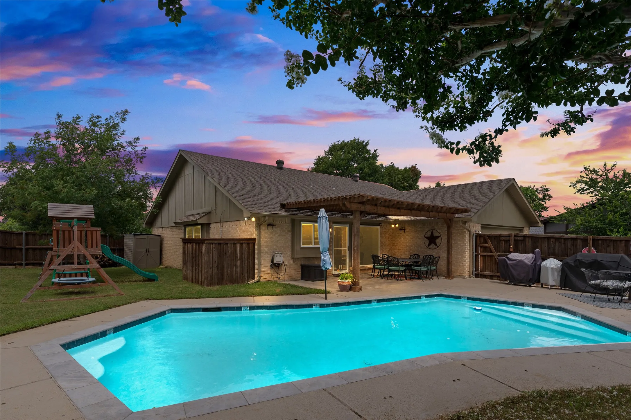 Expansive backyard featuring a built-in swimming pool with decking, a covered patio with a wood pergola, and a grassy area for pets or play!