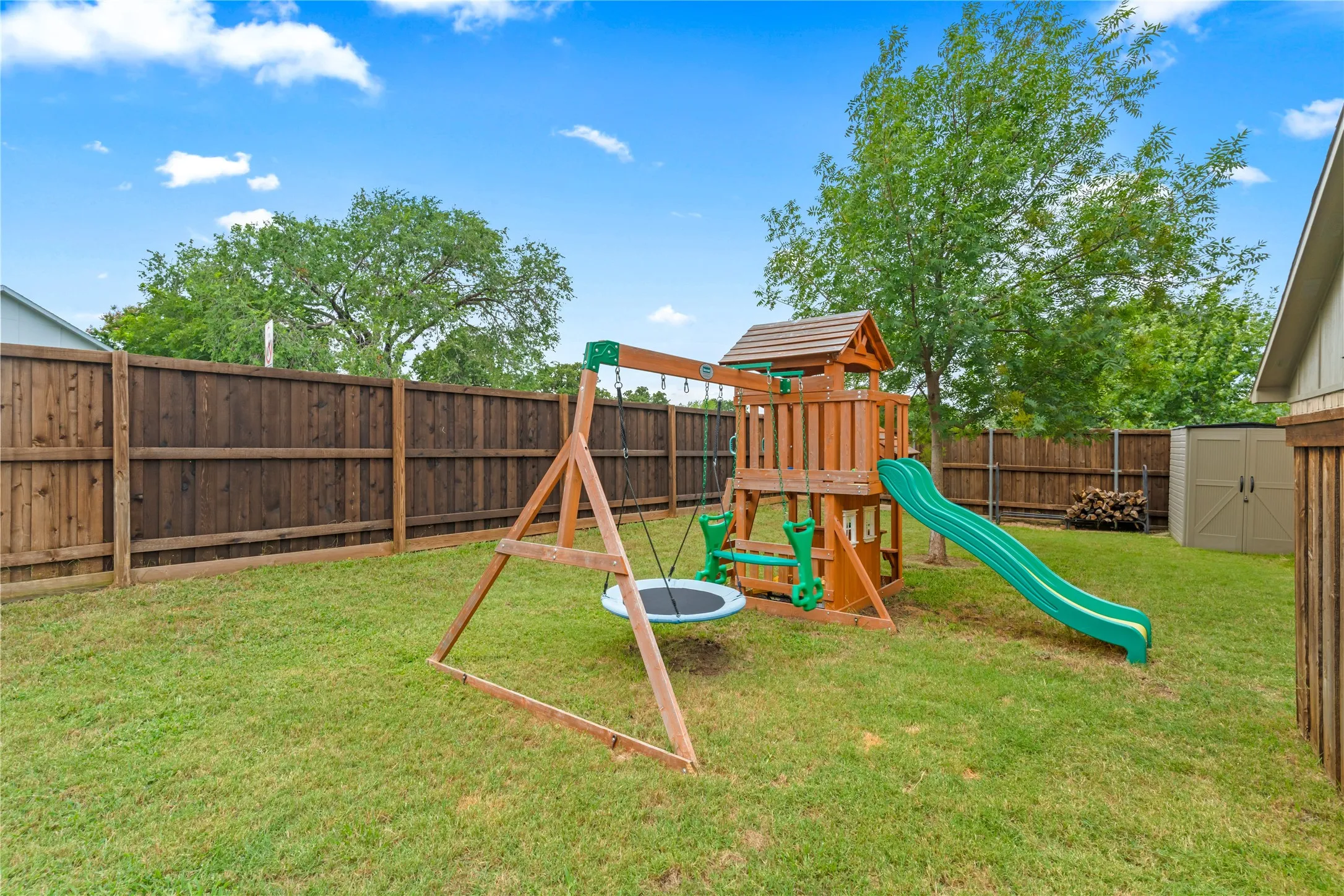 Fenced backyard with a grassy lawn, mature trees, and an outdoor storage shed