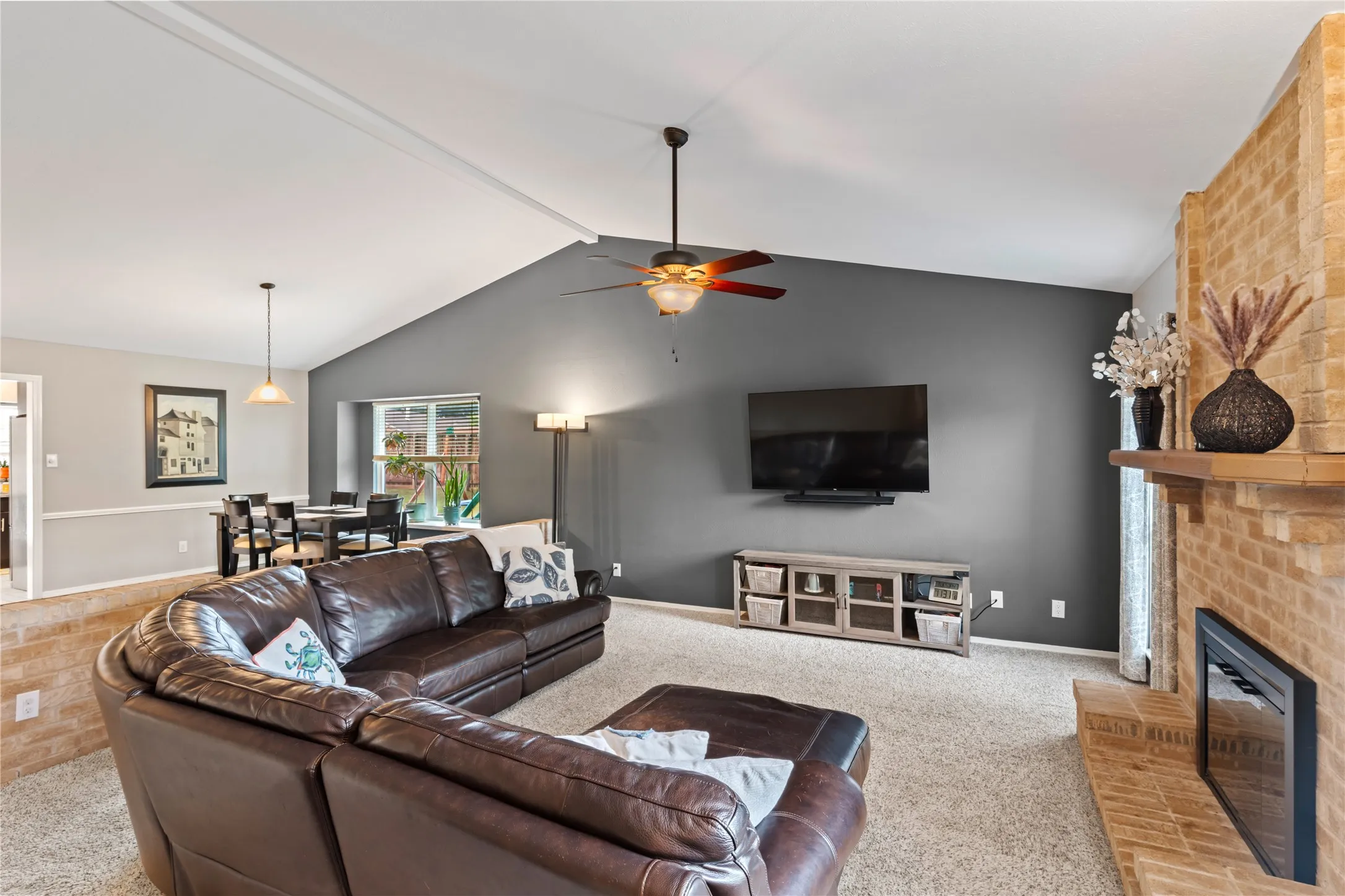 Vaulted ceilings, a substantial brick fireplace, and a ceiling fan with integrated lighting