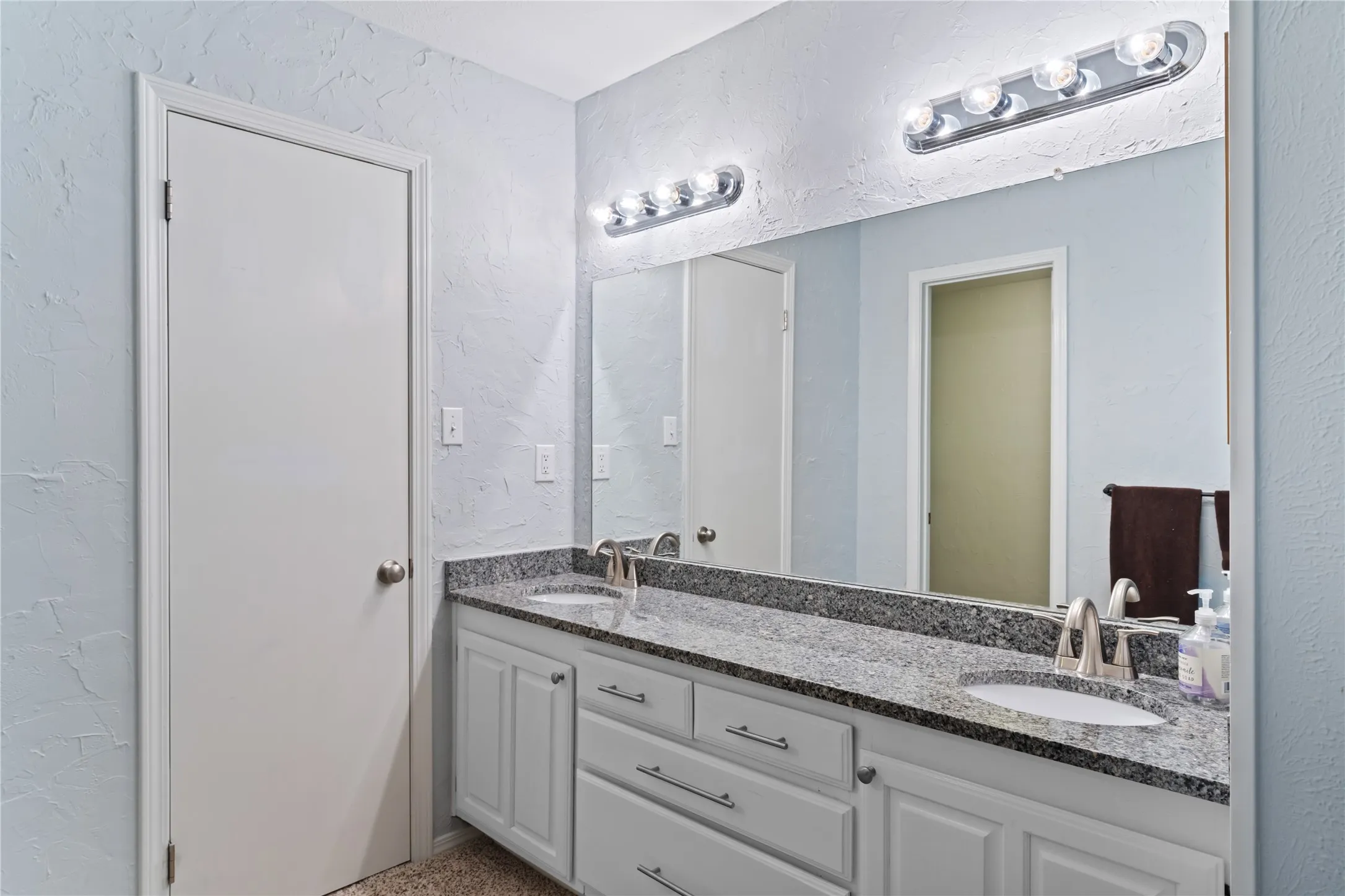 Double vanity with integrated sinks, granite countertop, chrome fixtures, white cabinetry, and vanity lighting