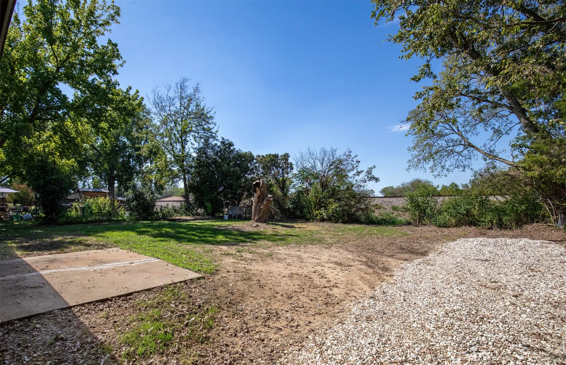 Expansive outdoor space featuring a concrete patio, a gravel area, and mature trees