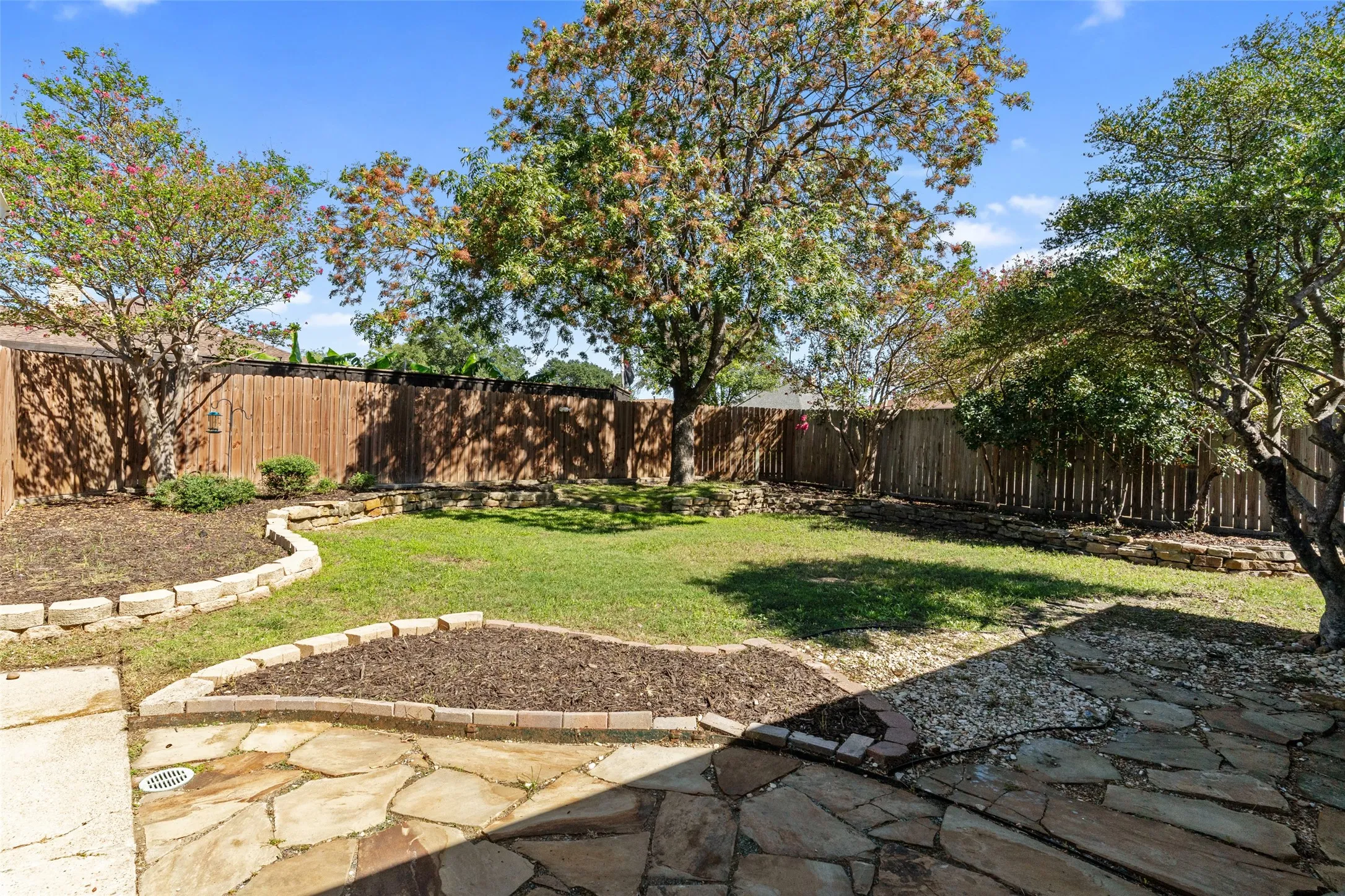 Expansive backyard featuring a natural stone patio, wood privacy fencing, and established trees