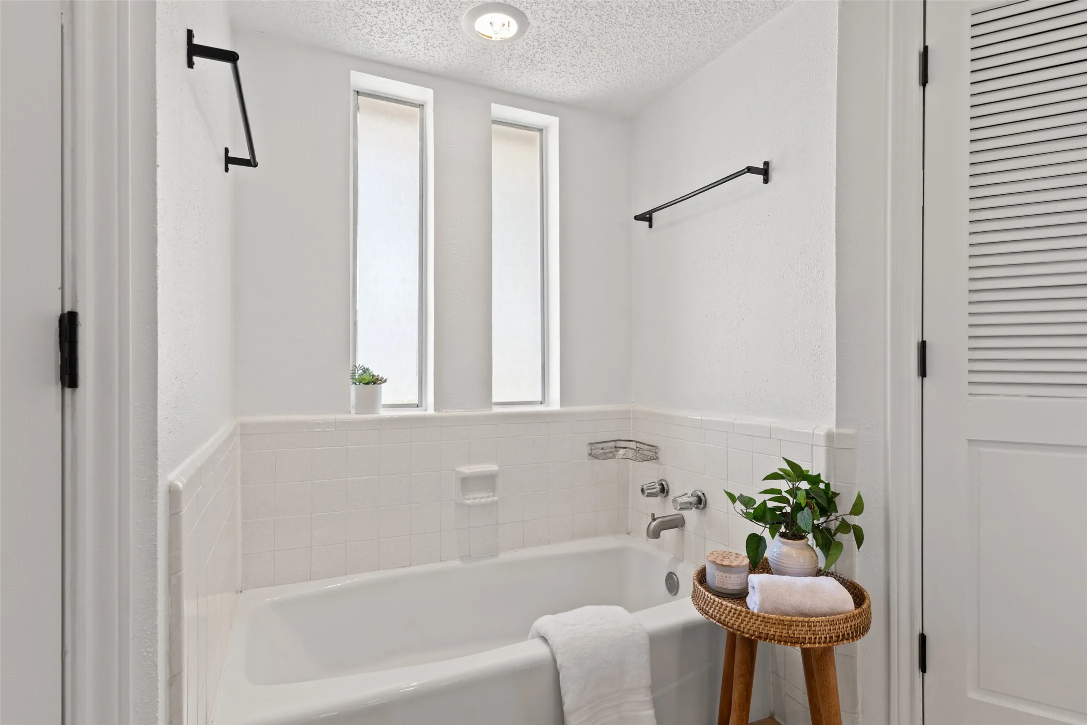 Bathtub with white tile surround, chrome fixtures, and two vertical privacy windows