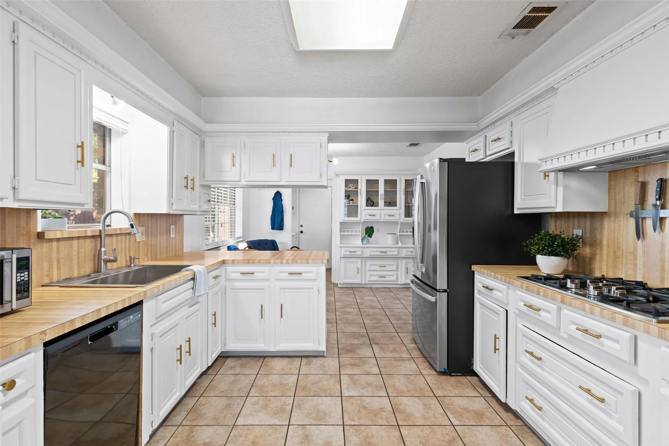 White cabinetry with gold-tone hardware, wood-finish countertops, tiled flooring, stainless steel appliances, and a built-in range with a ventilation hood