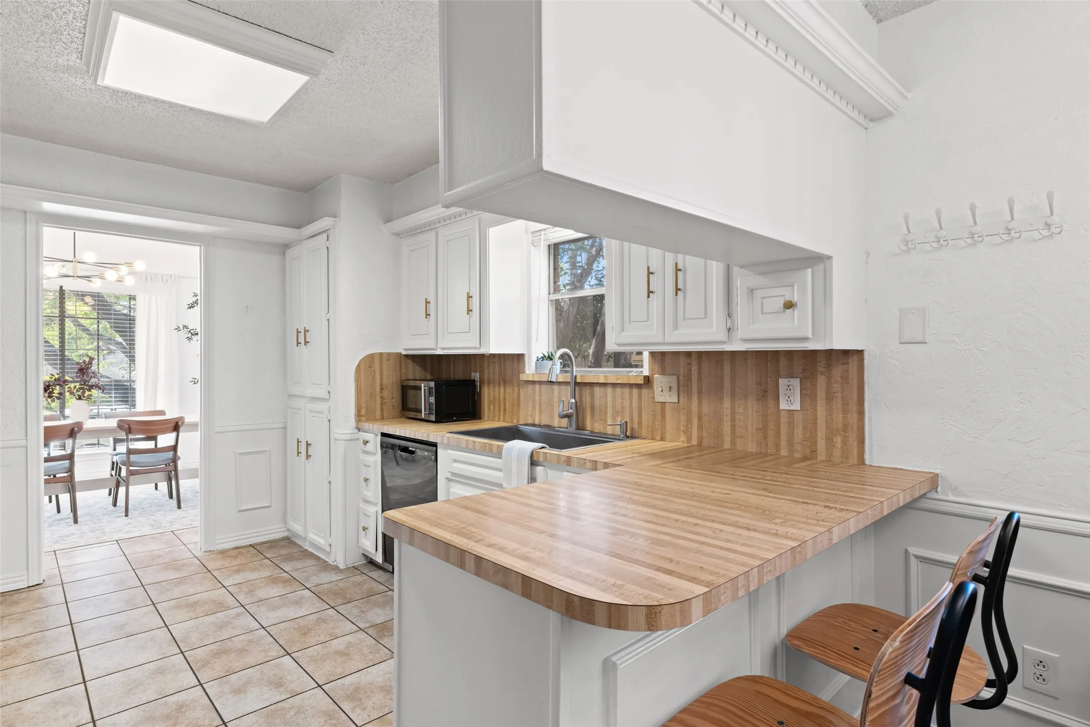 Kitchen with tile flooring, white cabinetry, a wood-finish countertop, and a built-in dishwasher
