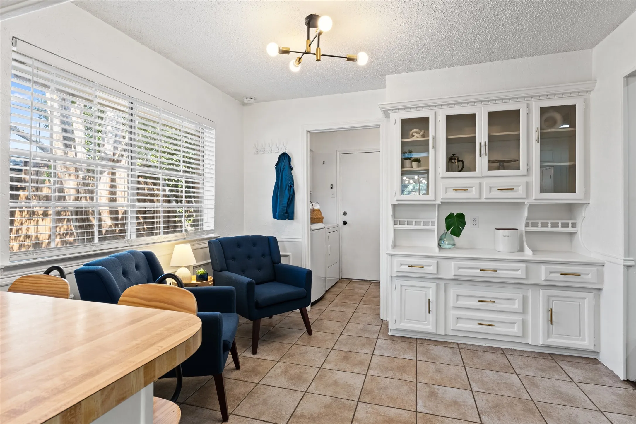 Built-in white hutch with glass-front cabinetry, neutral tile flooring, and a large window with blinds