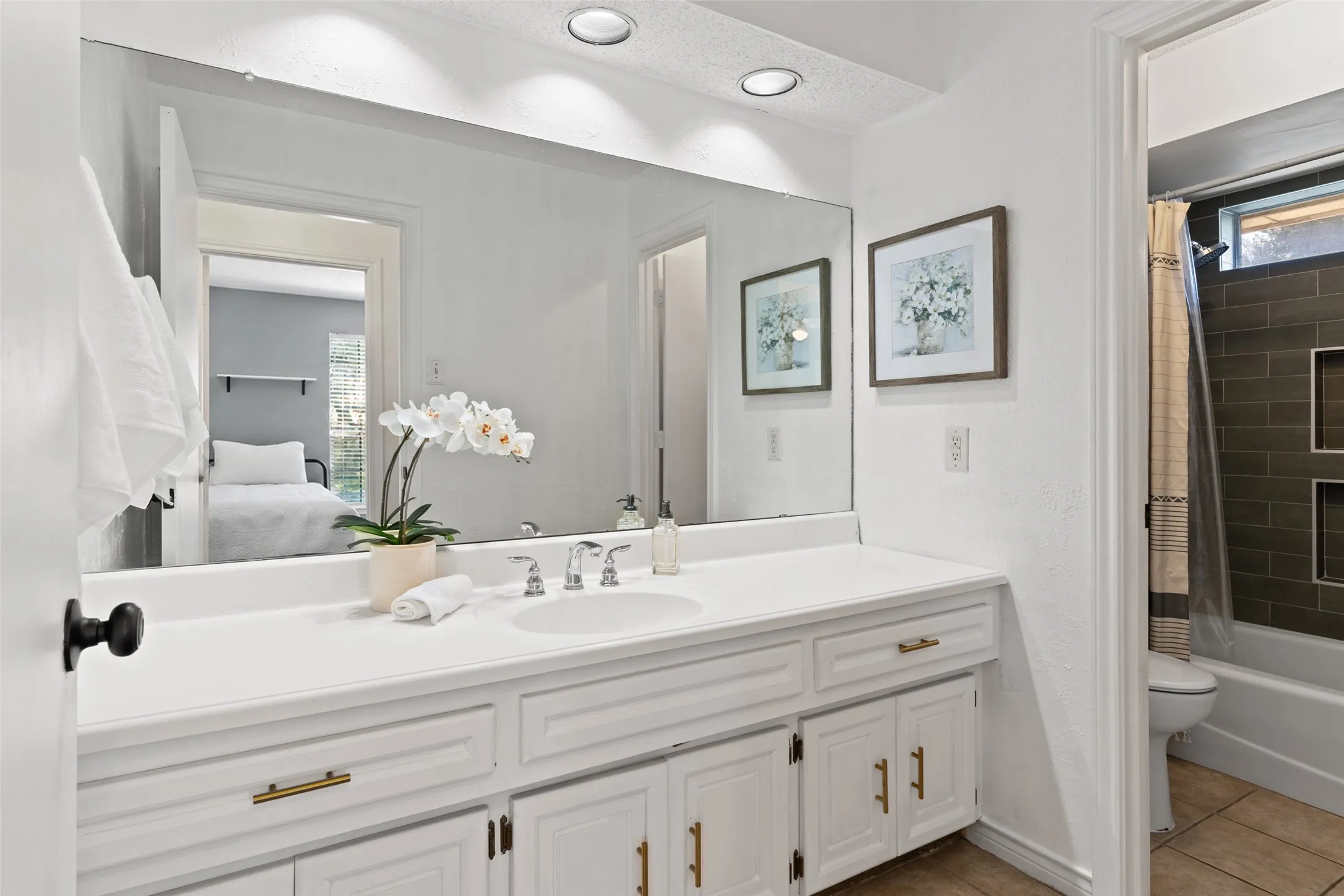 White vanity with brass hardware, undermount sink, and expansive wall-mounted mirror