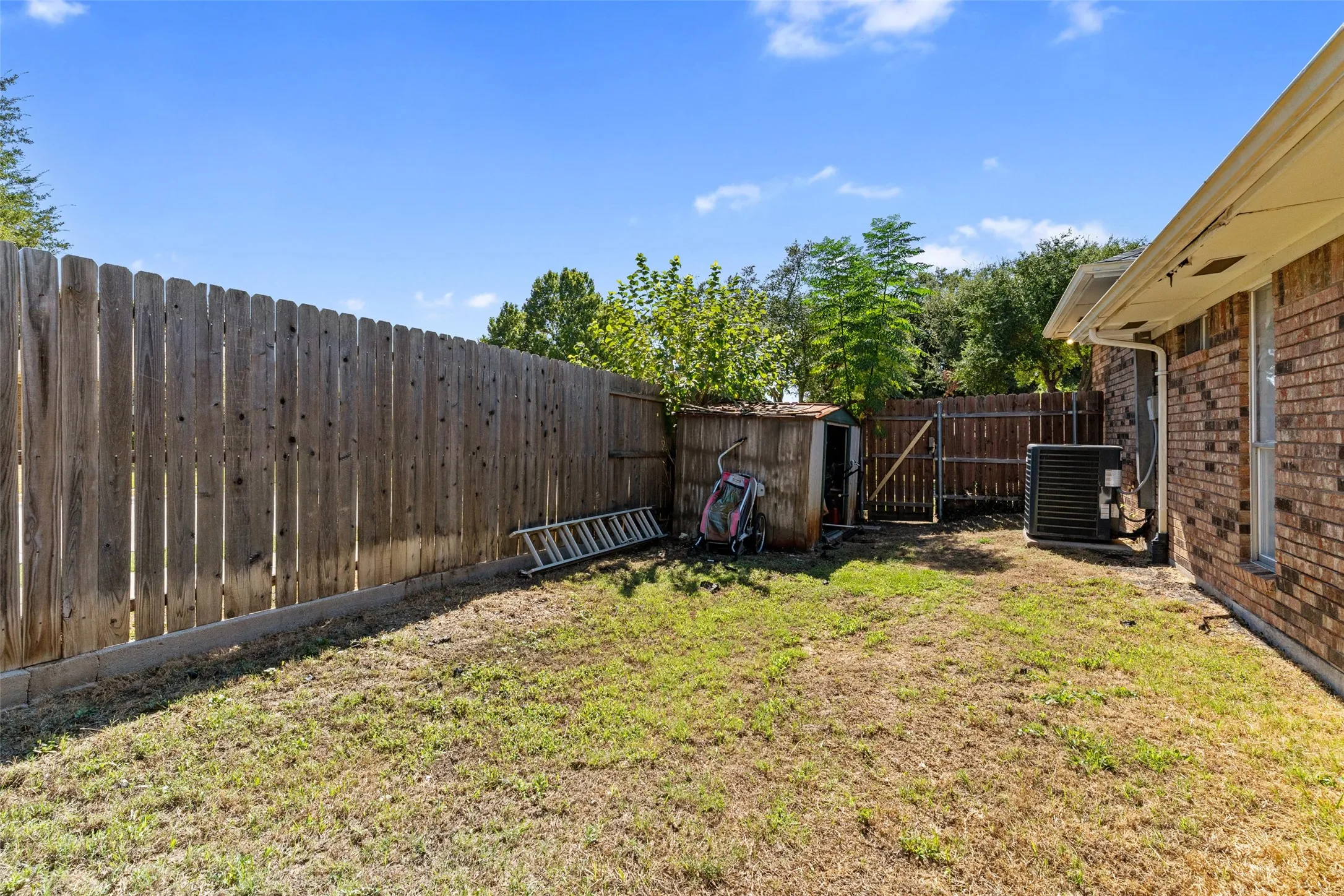 Expansive backyard featuring a wood fence, a small storage shed, and a brick exterior wall
