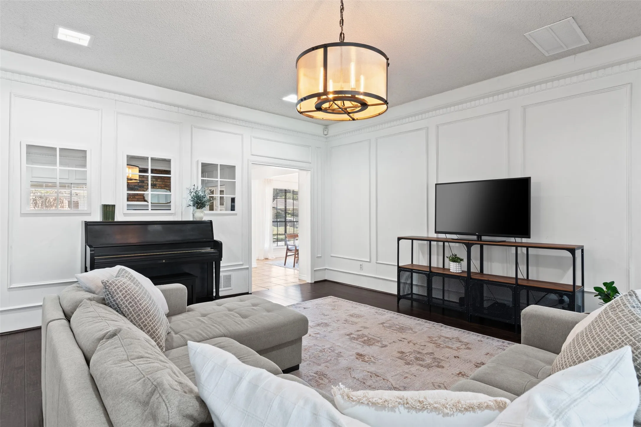 Sophisticated living room showcasing elegant architectural millwork, a pendant light fixture with brass accents, dark wood-finish flooring, and a built-in media console with open shelving