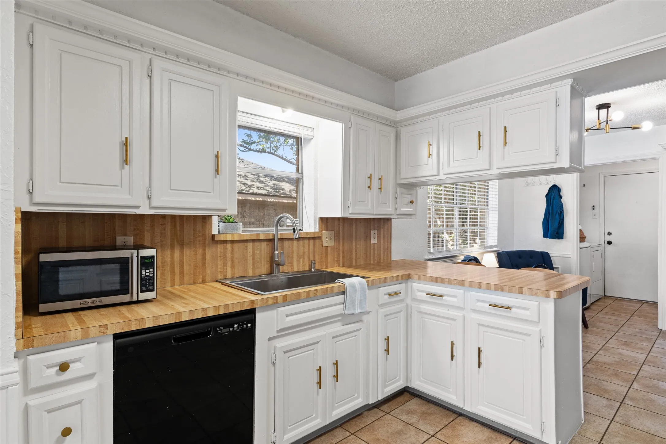 White cabinetry with gold-finish hardware, wood-finish countertops, stainless steel sink with a chrome faucet, and integrated black dishwasher