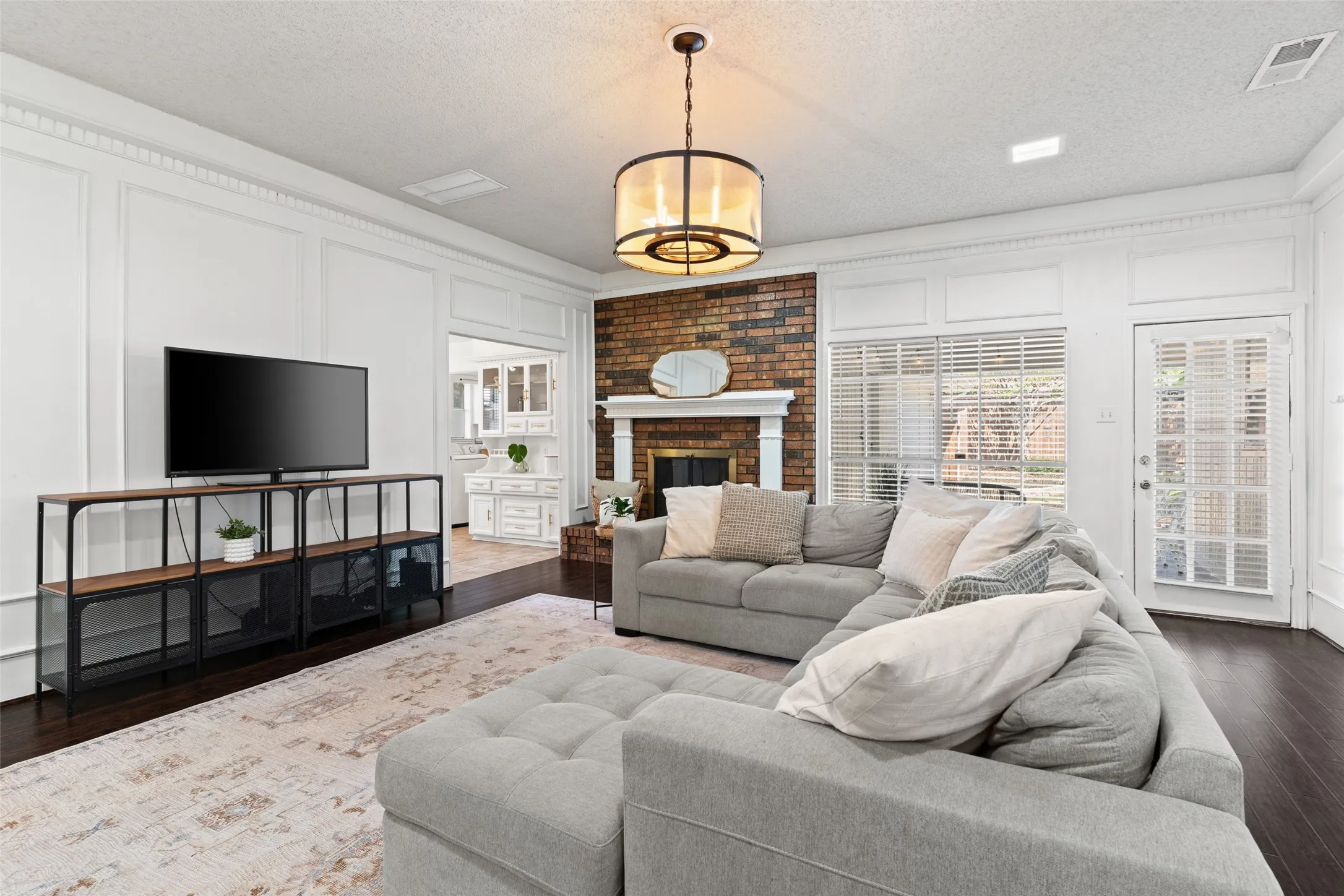 Hardwood flooring, brick fireplace with a white mantel, white paneled walls, and a glass-paned door