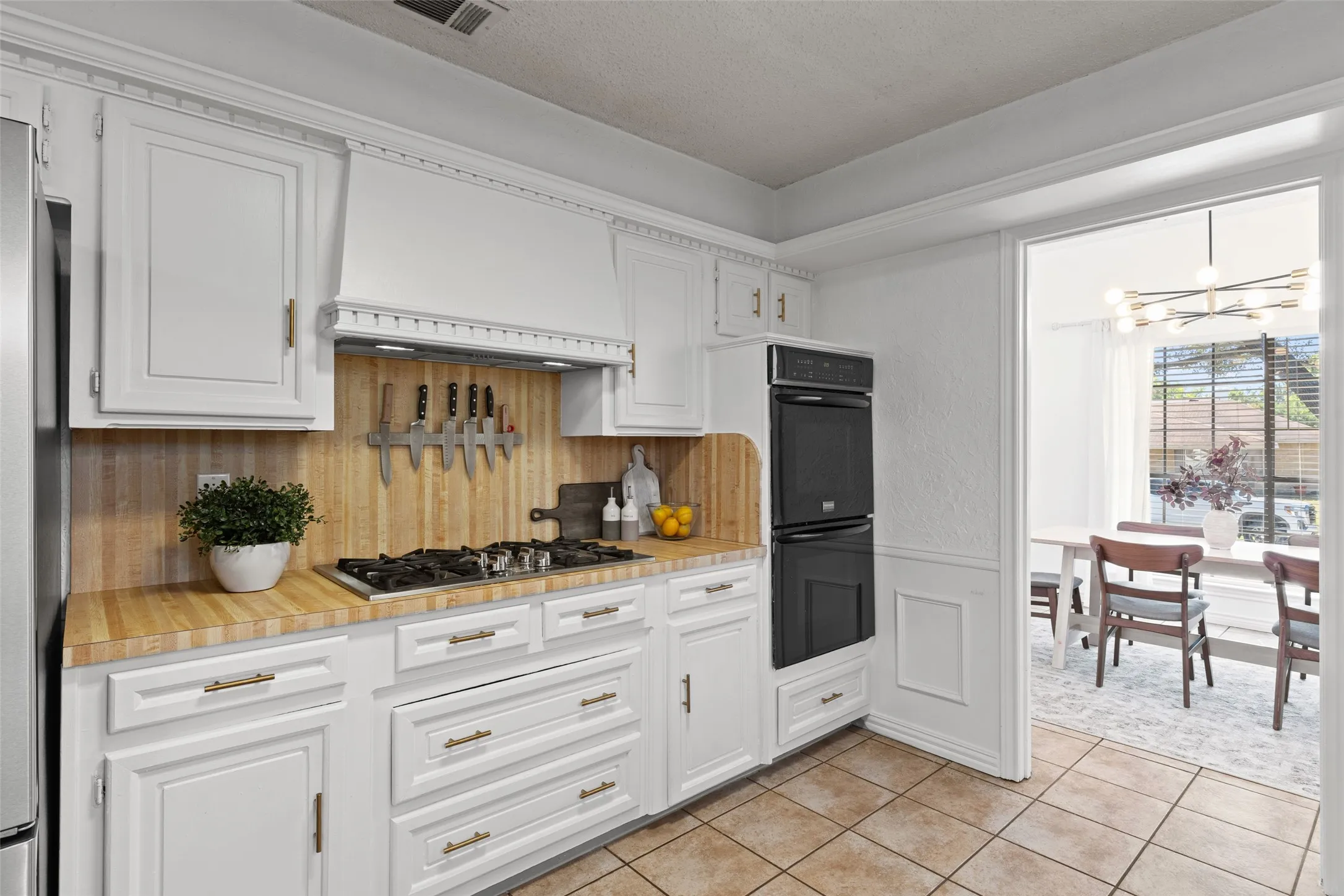 White cabinetry with gold-tone hardware, wood-finish countertops, tile flooring, and a built-in double oven