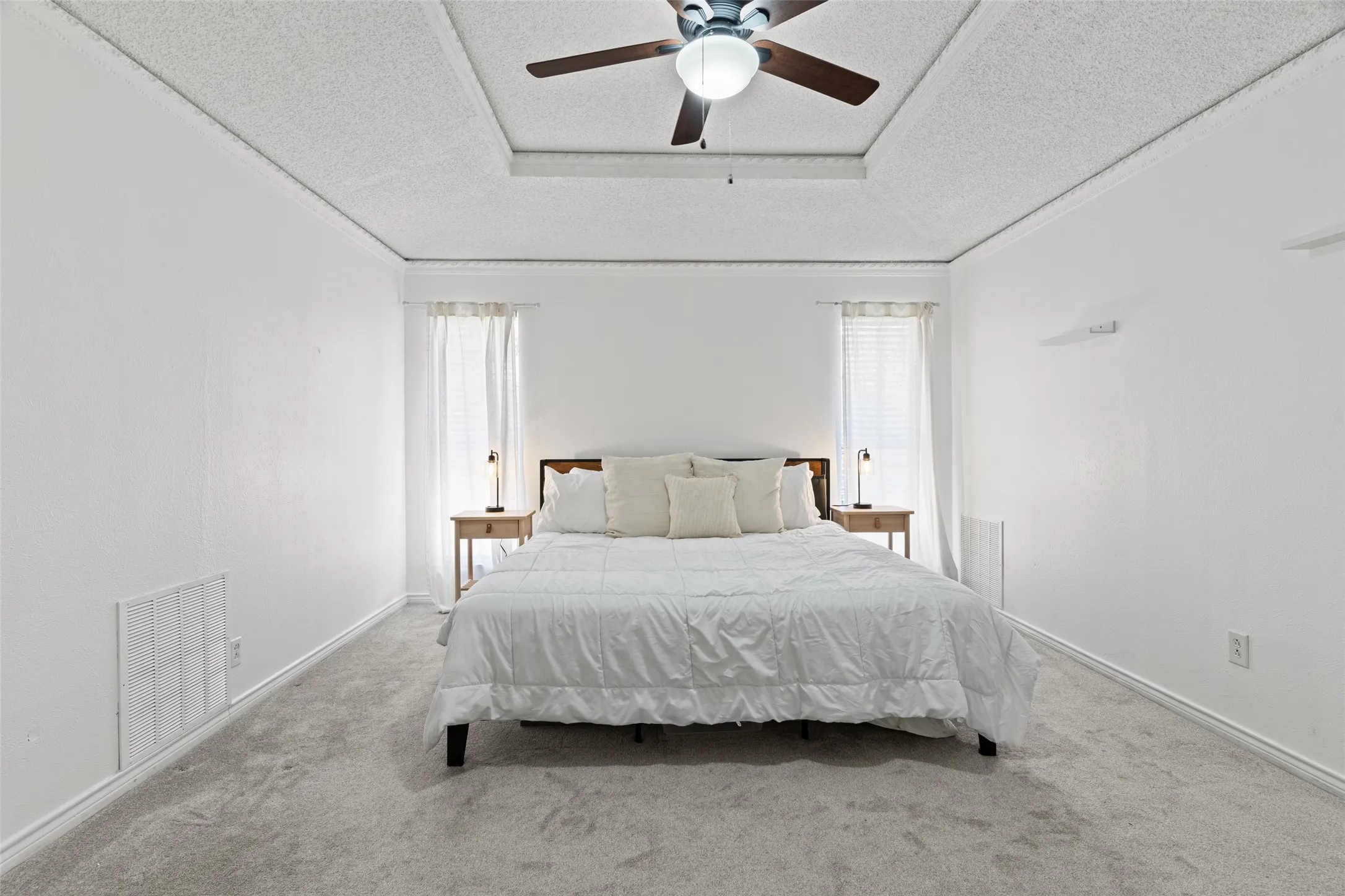 Spacious primary bedroom with soaring coffered ceilings, ceiling fan with integrated lighting, and abundant natural light from dual windows