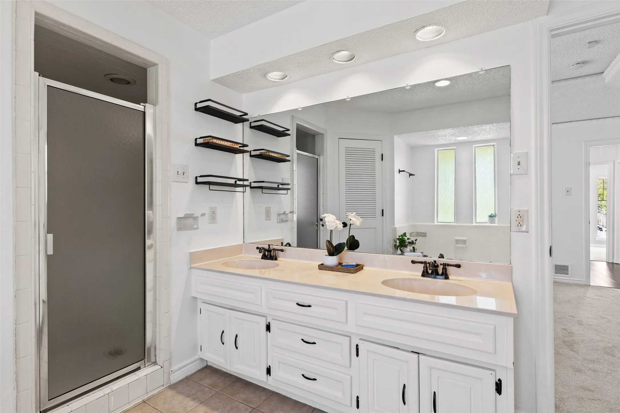 Dual vanity with integrated sinks, recessed lighting, expansive wall mirror, and built-in shelving