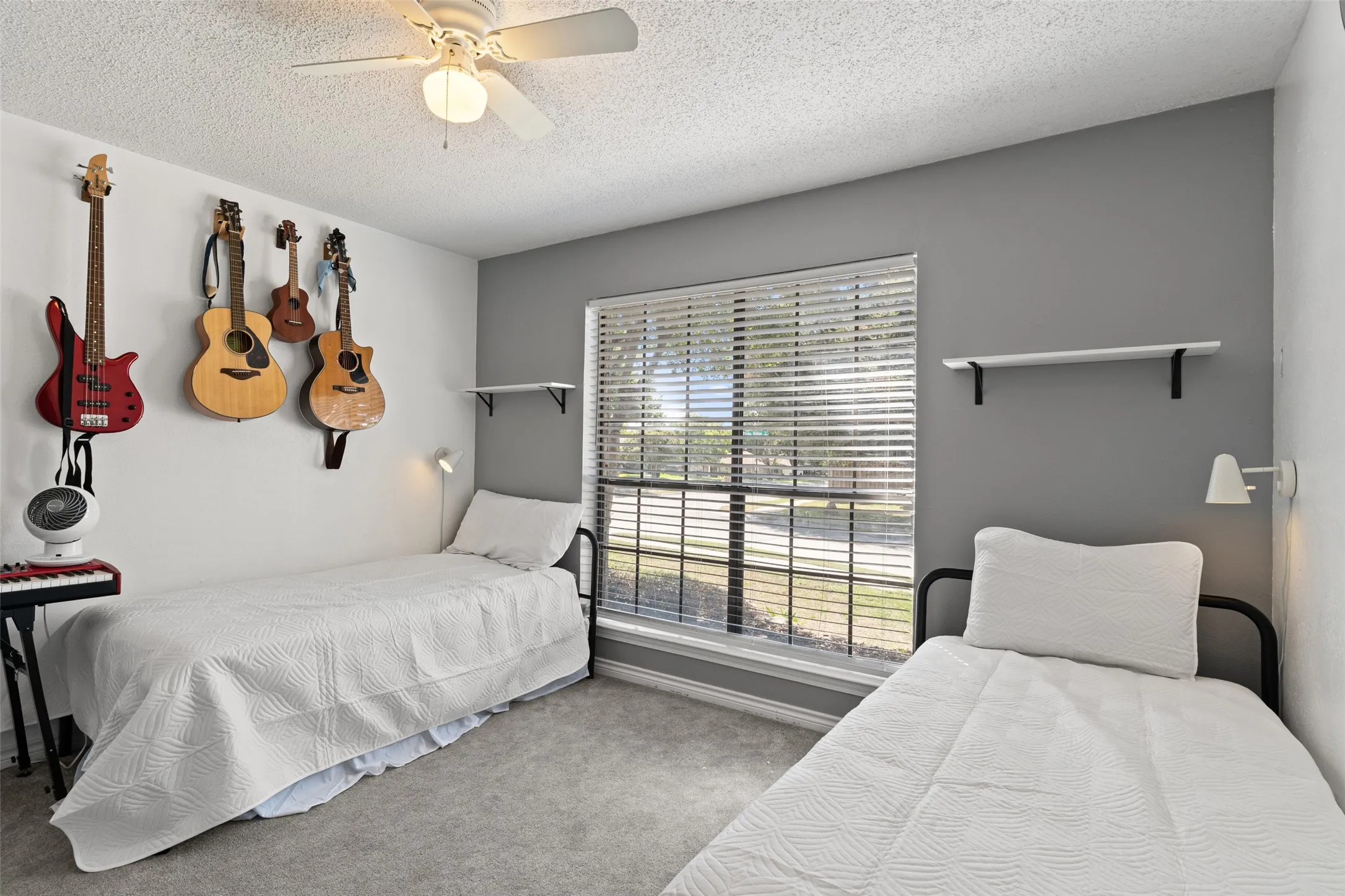 Textured carpeting, window with horizontal blinds, built-in wall shelving, and ceiling fan with integrated lighting
