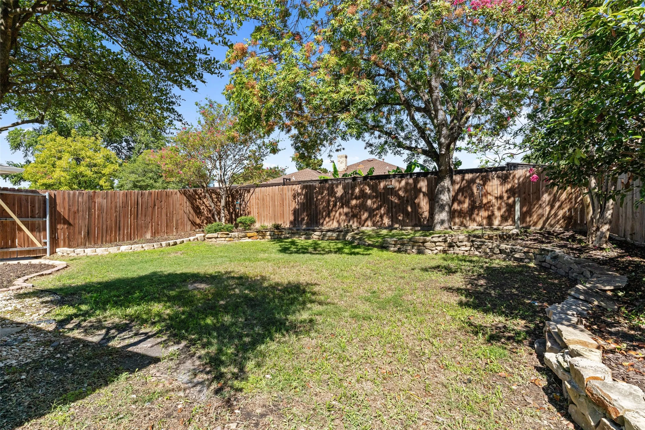 Expansive yard featuring a wood privacy fence, stone retaining walls, mature trees, and a wooden gate