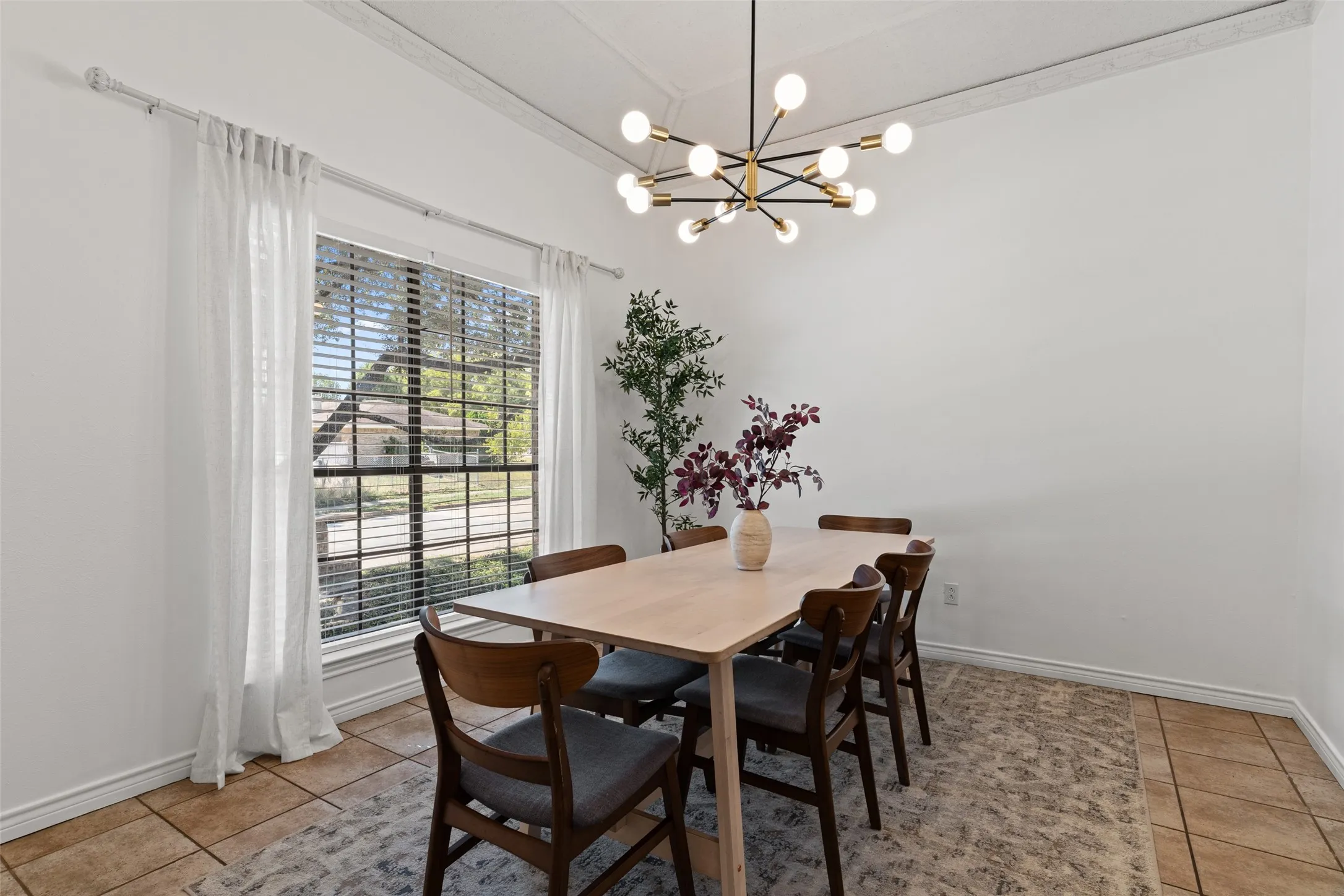 Recessed ceiling with decorative trim, contemporary chandelier, large window with blinds, and tile flooring