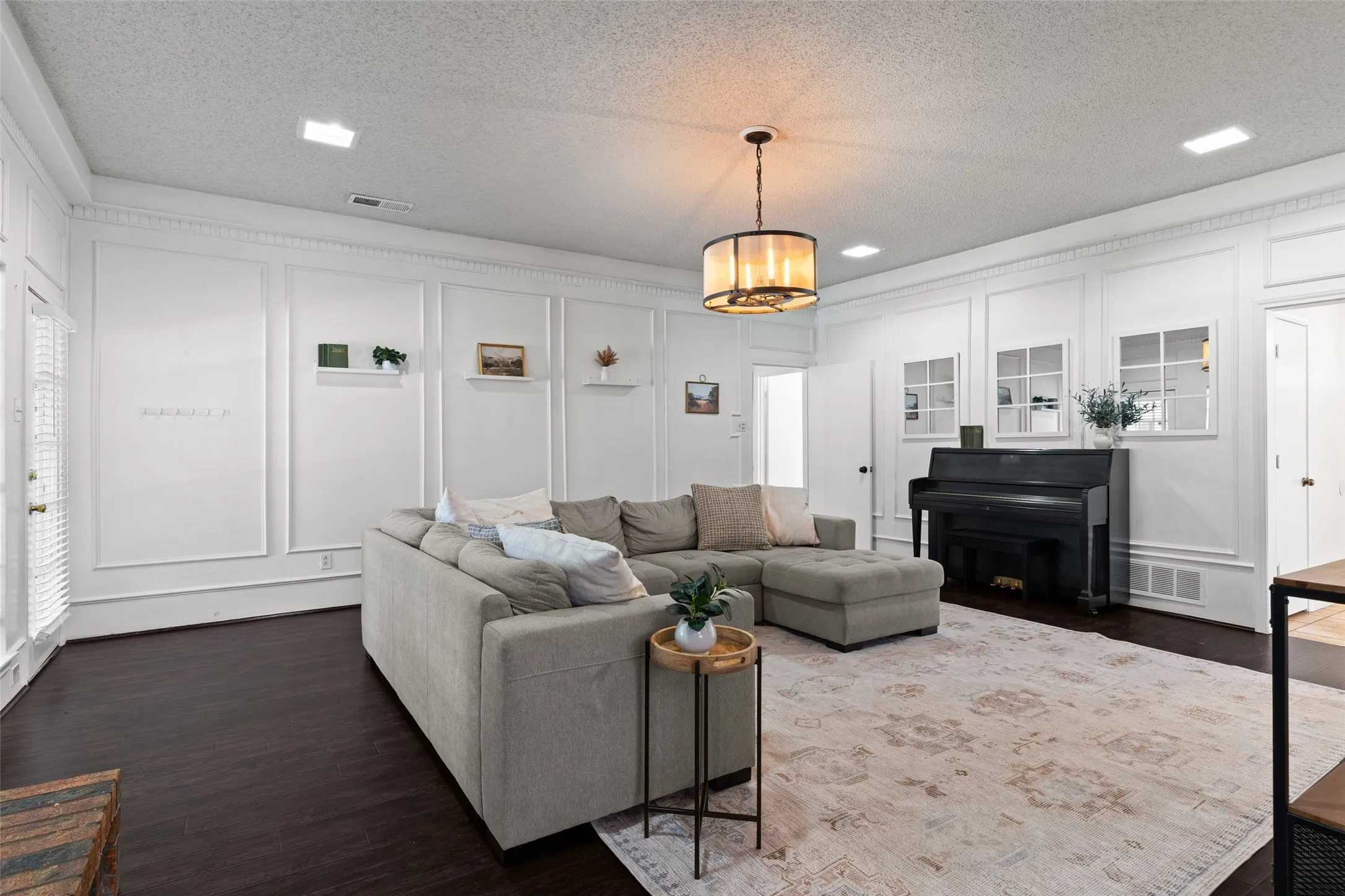 Living area featuring dark wood-finish flooring, white panel molding, recessed lighting, and a drum-style chandelier