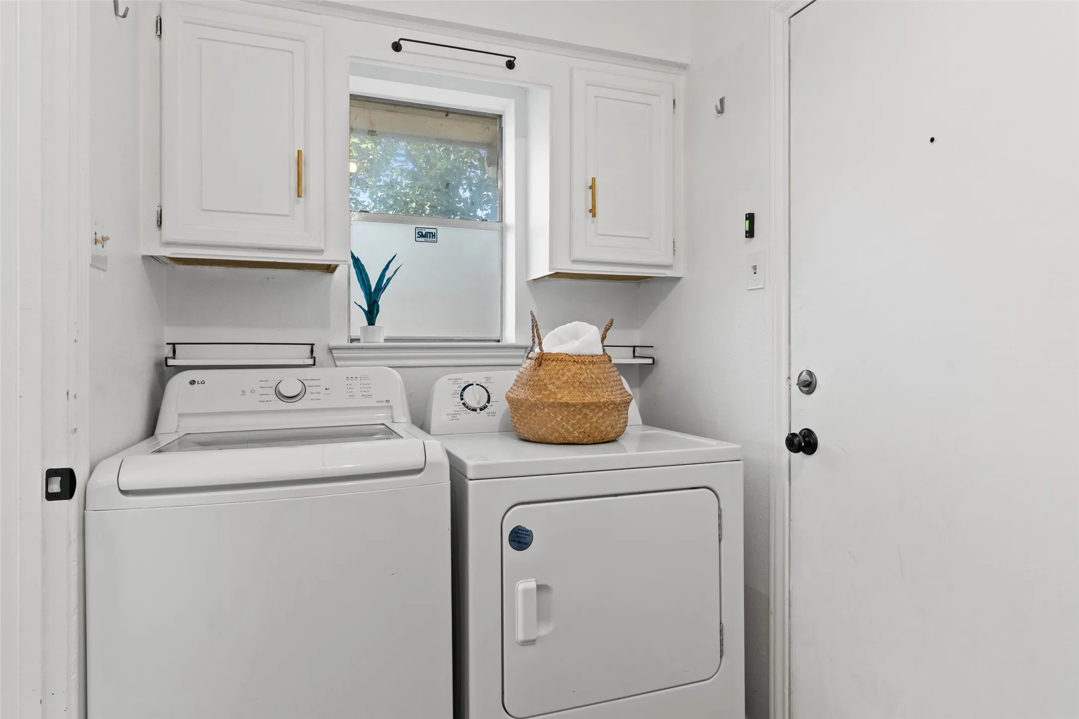 White painted cabinetry with gold-tone hardware, a window offering natural light, and a white entry door with a black knob