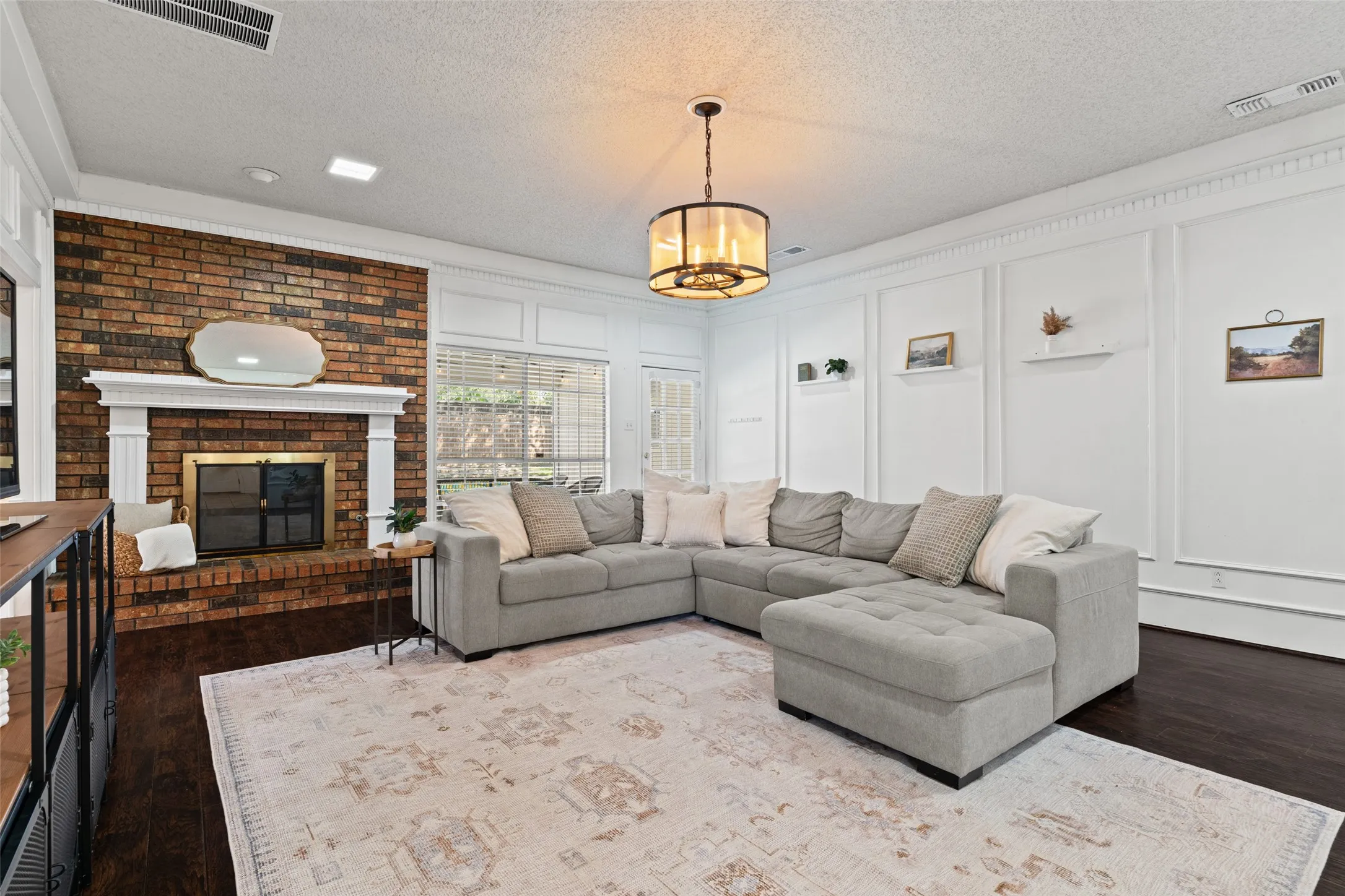 Brick fireplace with a white mantel, dark wood-finish flooring, white panel molding, and a drum-style ceiling fixture