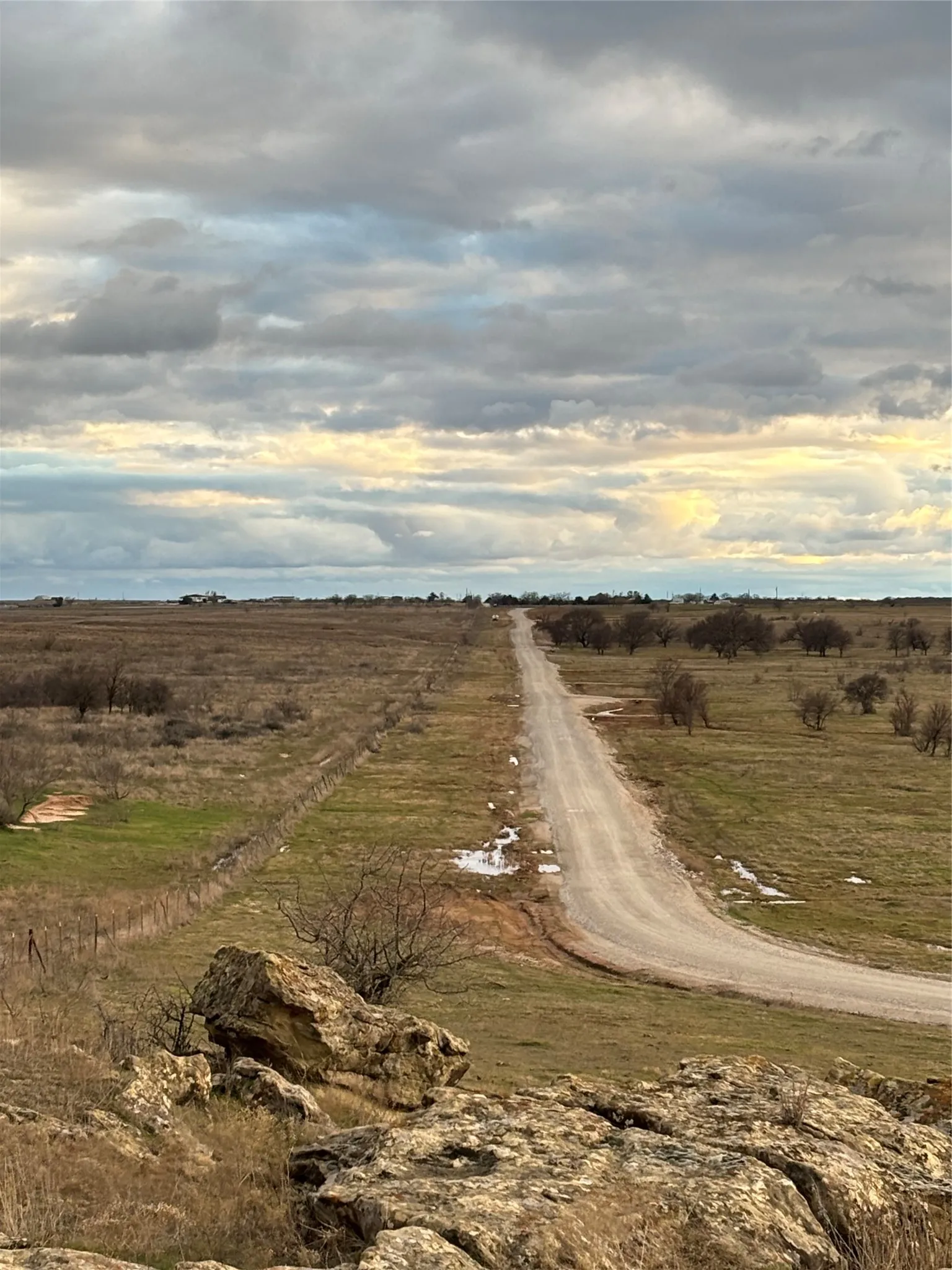 Expansive land featuring a long gravel road, natural rock formations, and scattered trees across the terrain