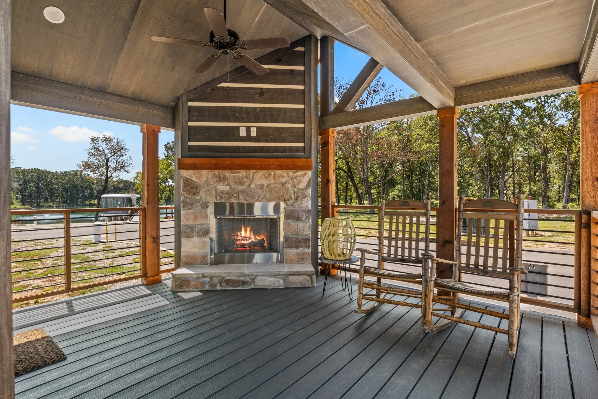 Deck with an outdoor stone fireplace, ceiling fan, and view of wooded area