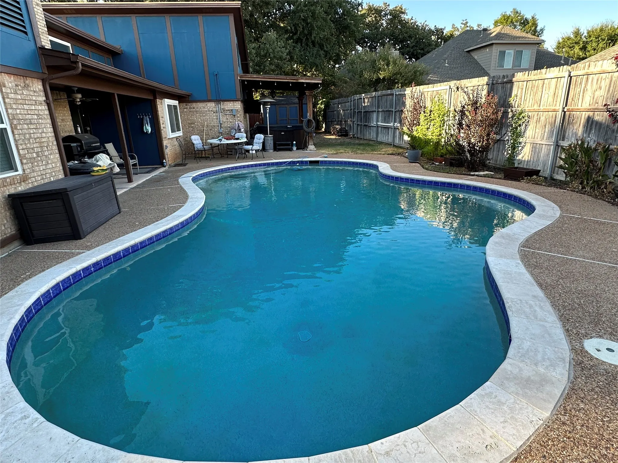 Freeform swimming pool with blue tile accents, concrete decking, and an adjacent covered patio area