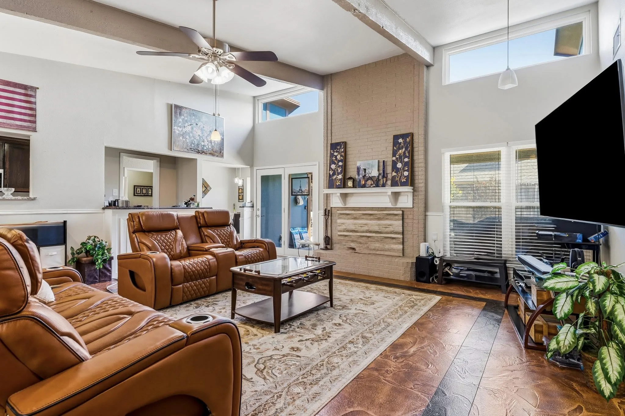 Vaulted ceiling with exposed beams, brick fireplace with mantel, ceiling fan with illumination, French doors, and high transom windows
