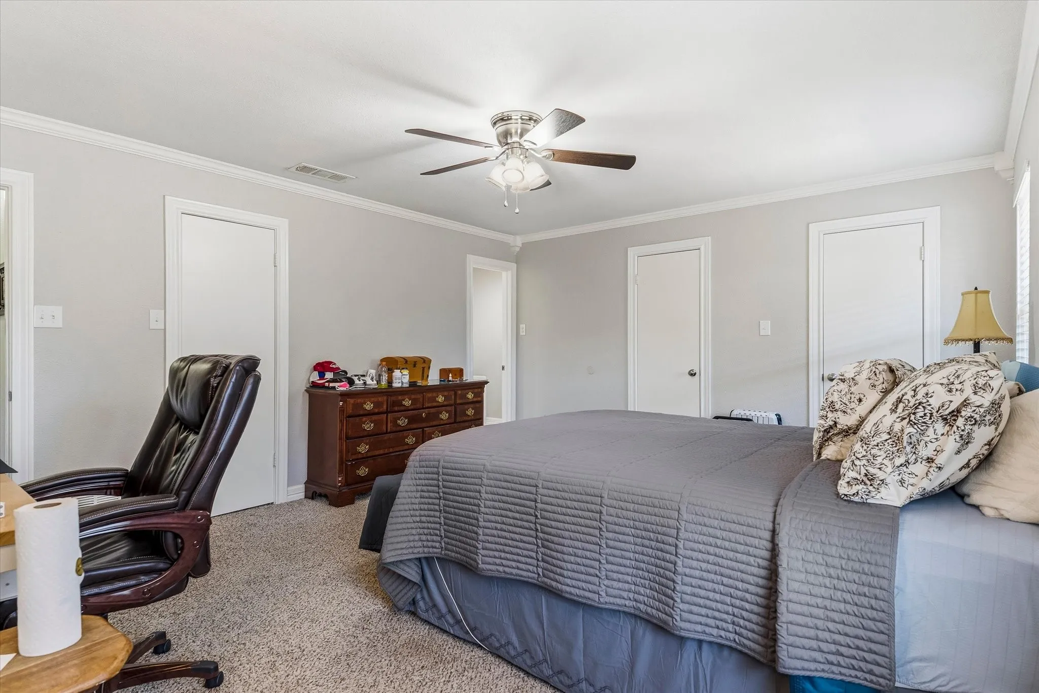 Textured carpet flooring, ceiling fan with integrated lighting, crown molding, white painted trim, and multiple white panel doors