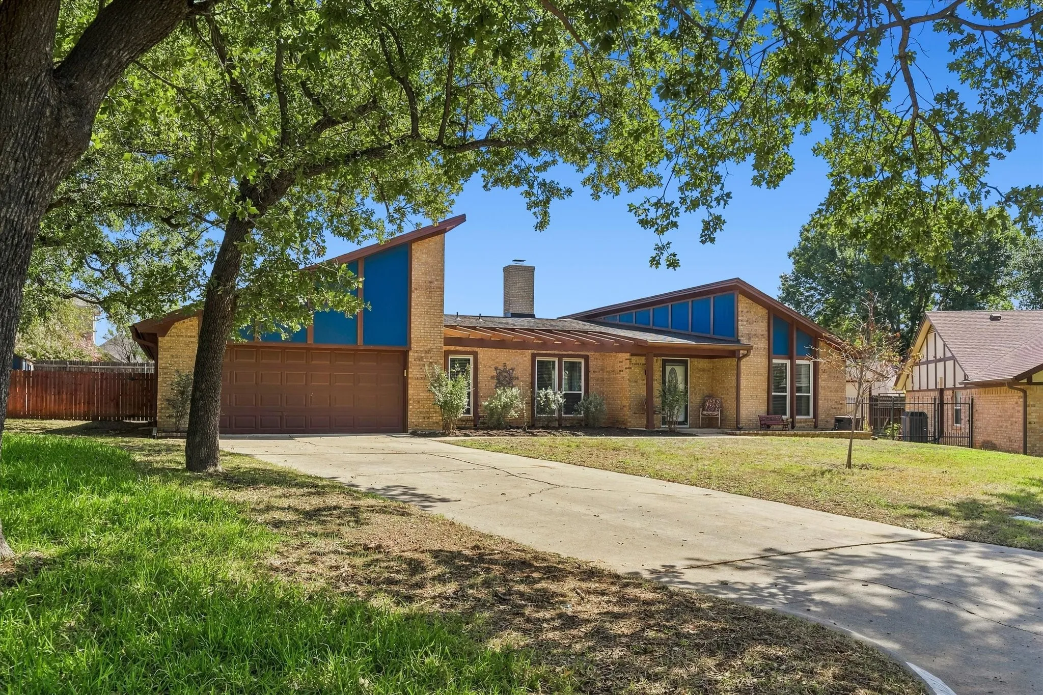 Brick exterior with a prominent chimney, large driveway, attached garage, and striking sloped roofline with blue-tinted windows