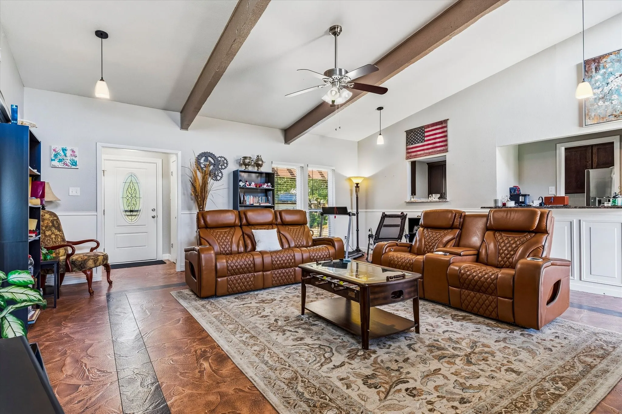 Vaulted ceiling with exposed beams and ceiling fan, wood-finish flooring, white paneled wainscoting, and a white entry door with decorative glass insert