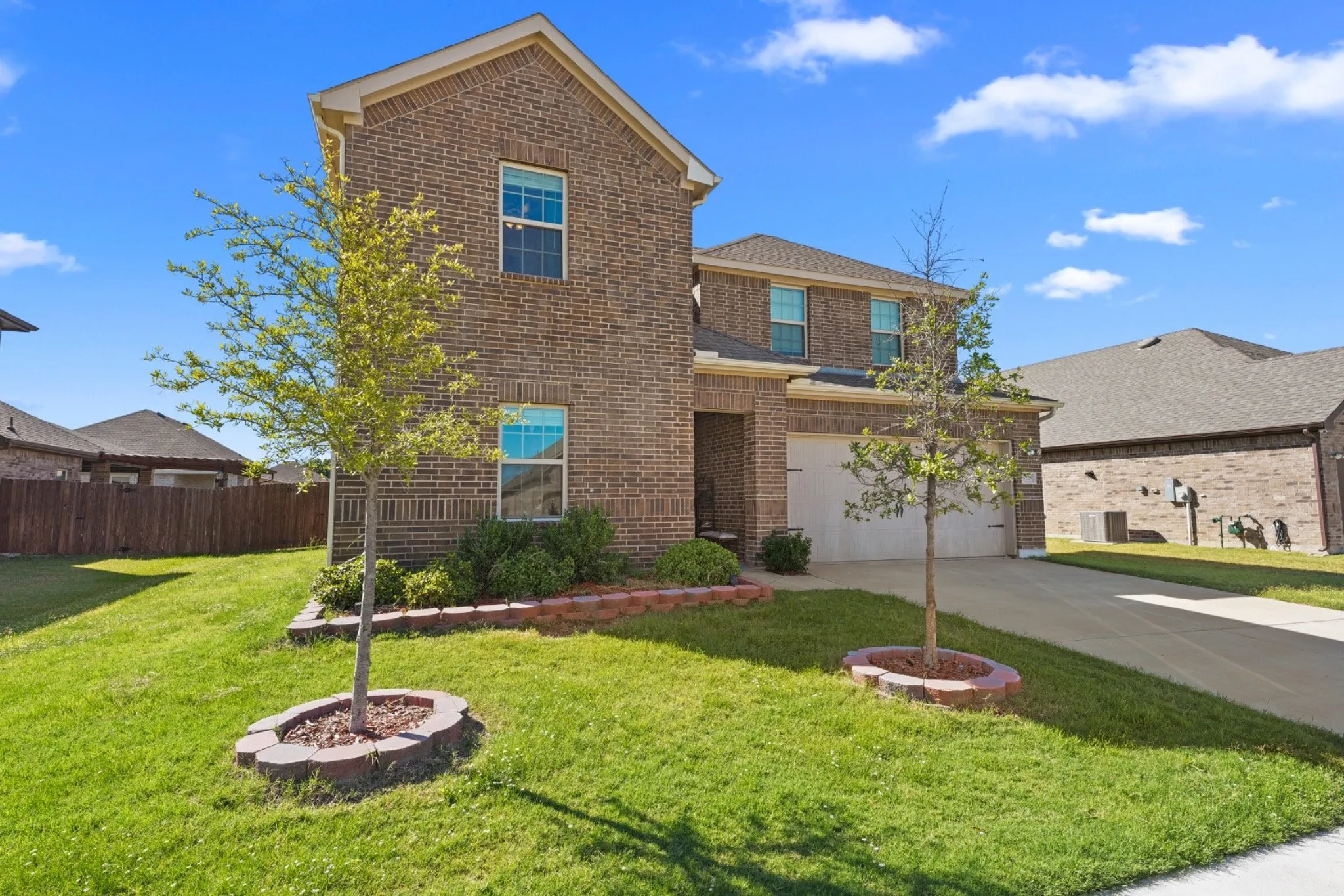 Brick exterior with multi-pane windows, attached garage, concrete driveway, and landscaped front yard with decorative brick edging