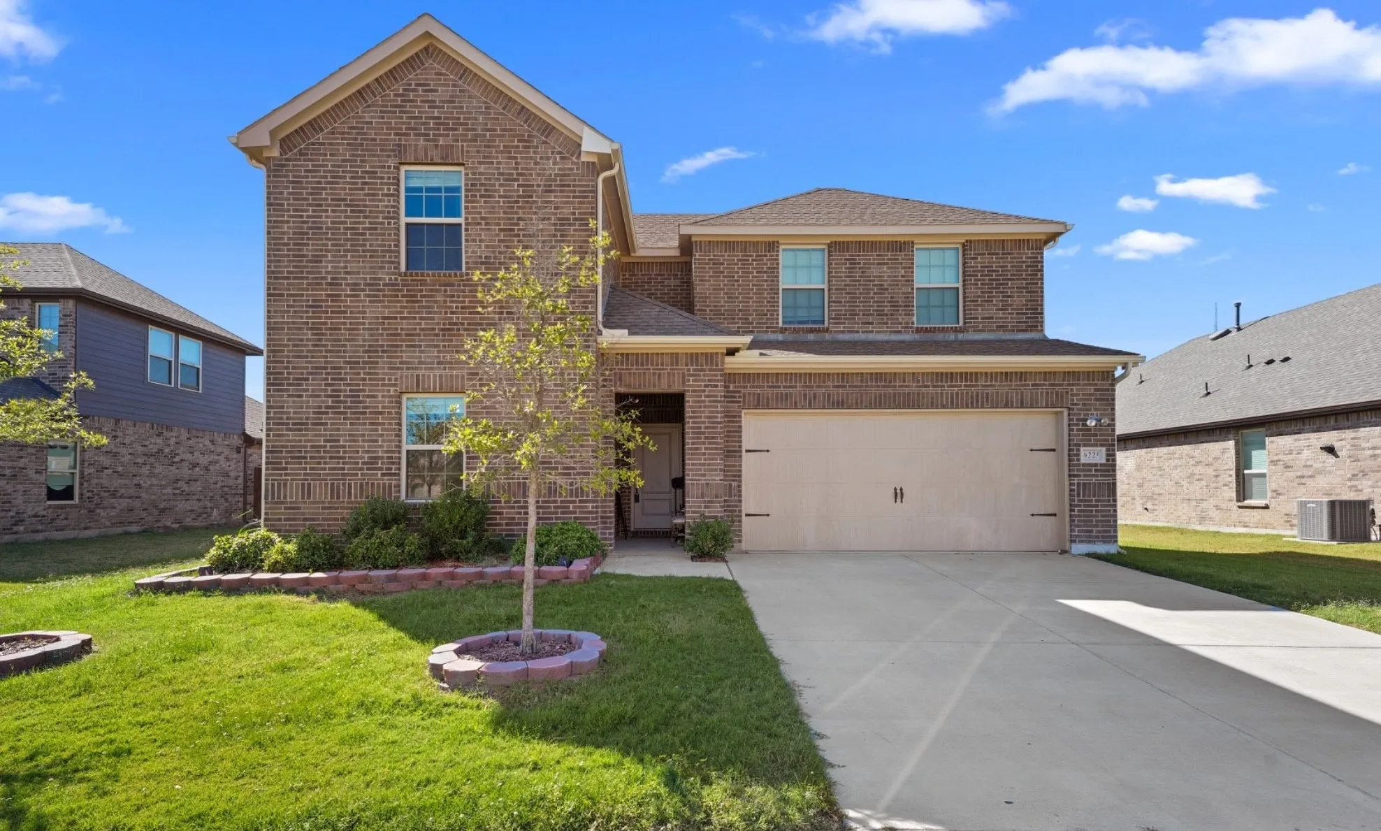Two-story brick exterior with a two-car garage, concrete driveway, and front lawn with decorative landscaping