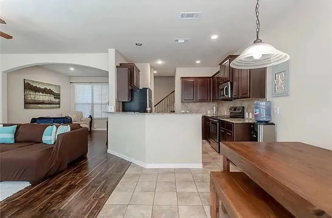Kitchen with decorative backsplash, dark brown cabinetry, hanging light fixtures, stainless steel appliances, and light stone counters