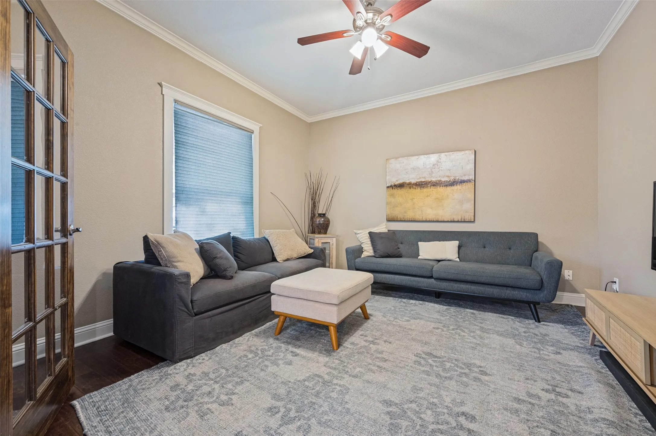 Hardwood flooring, crown molding, a ceiling fan, window treatments, and a wood-finish French door