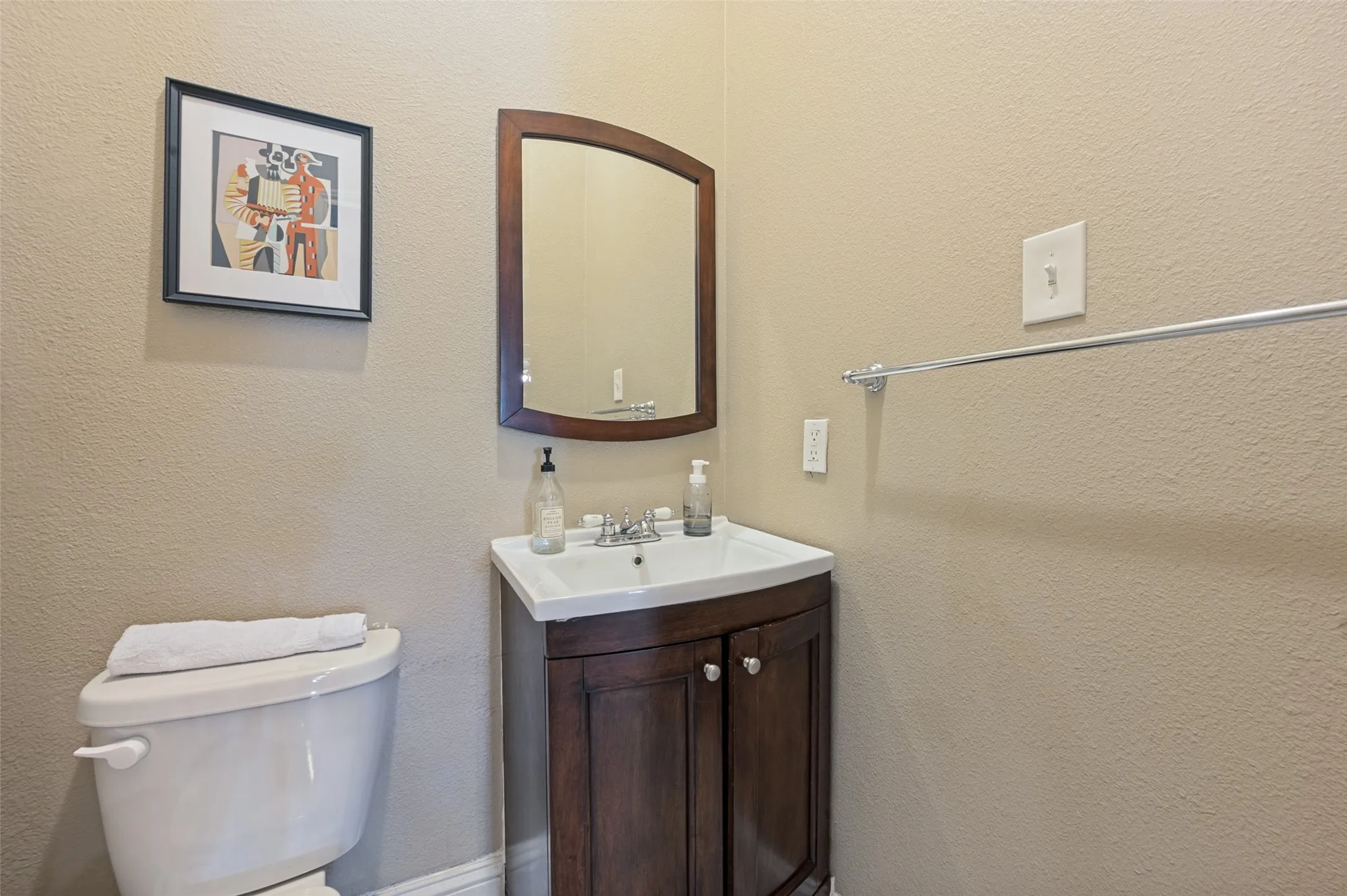 White toilet with a built-in tank, wood-finish vanity with dual-door storage, rectangular ceramic sink, and a wood-frame wall mirror