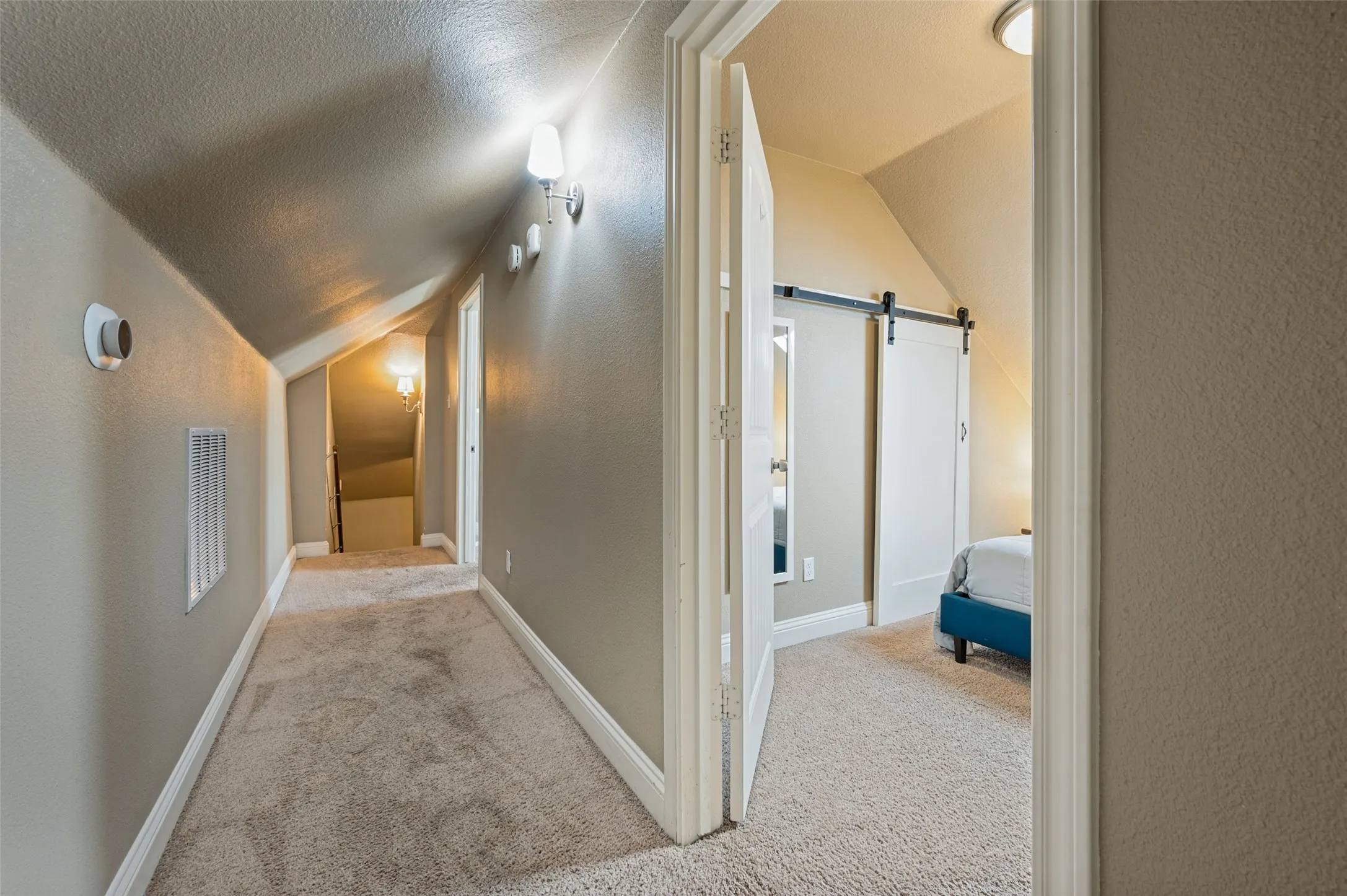 Carpeted hallway with sloped ceilings, white baseboards, and wall-mounted light fixtures